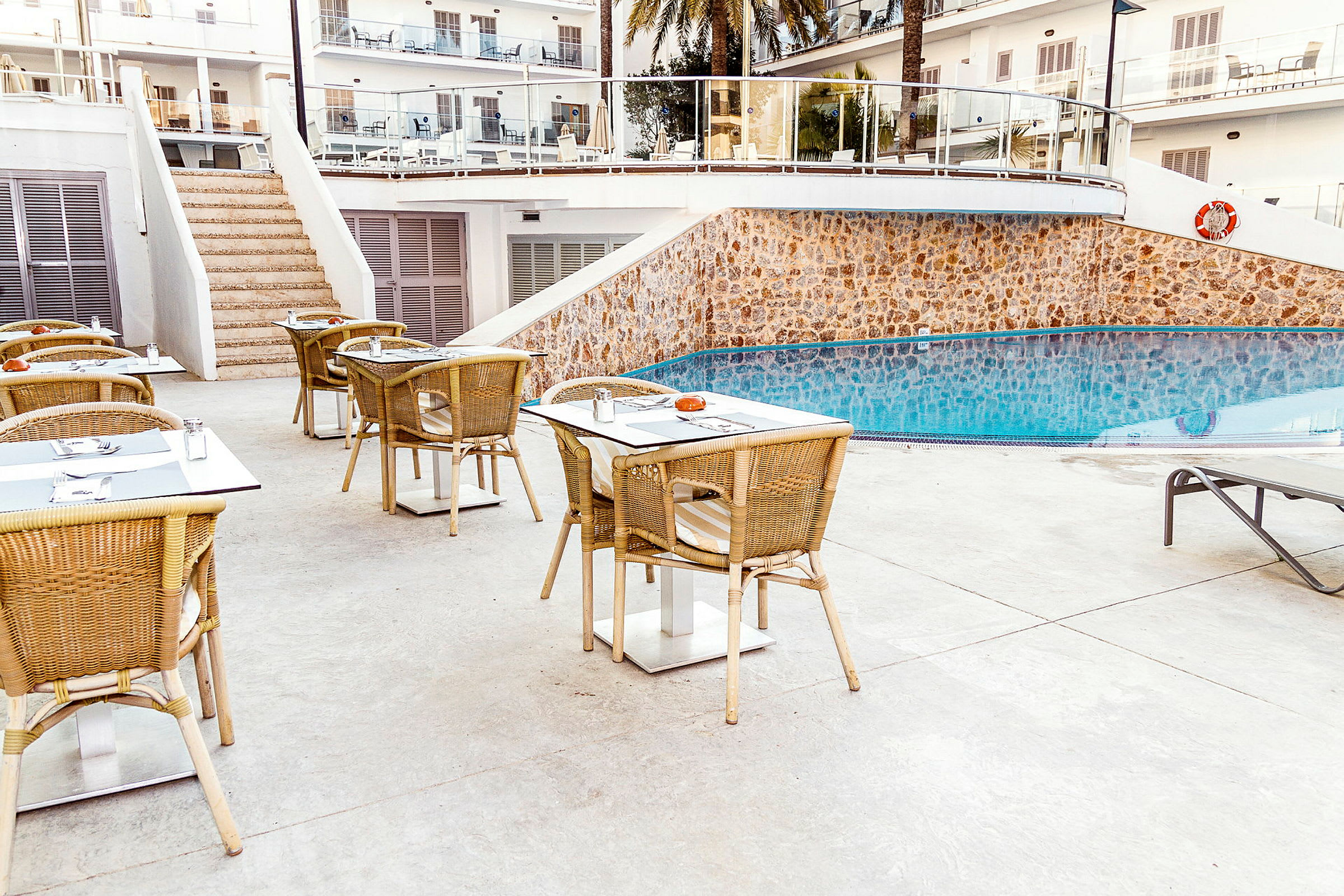 Utemöbler med bord och stolar vid en pool, omgivna av hotellbyggnader. (AI-genererad text)