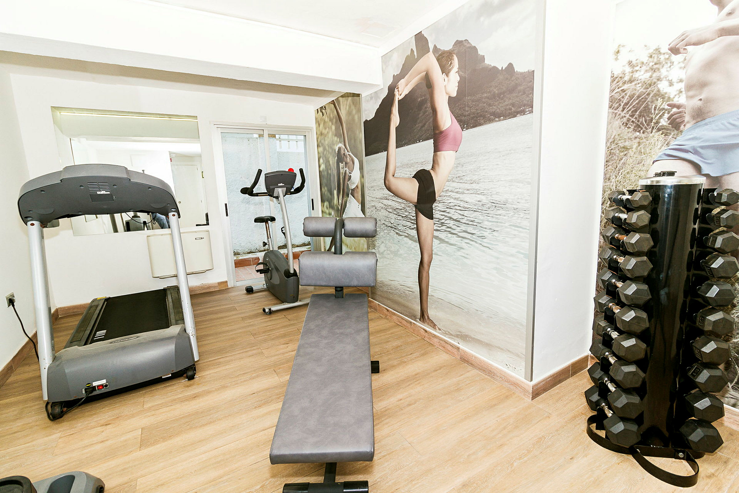 Ett litet gym med en träningscykel, ett löpband, en bänk och en ställning för hantlar. (AI-genererad text)