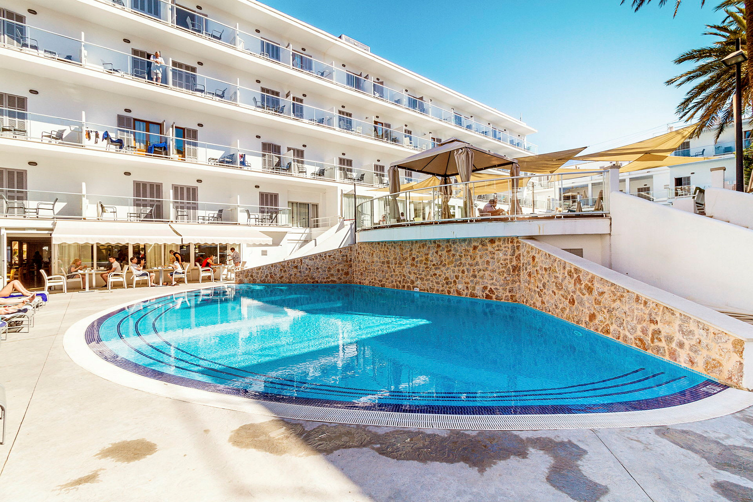 Utomhuspool vid hotell med solstolar och balkonger. (AI-genererad text)