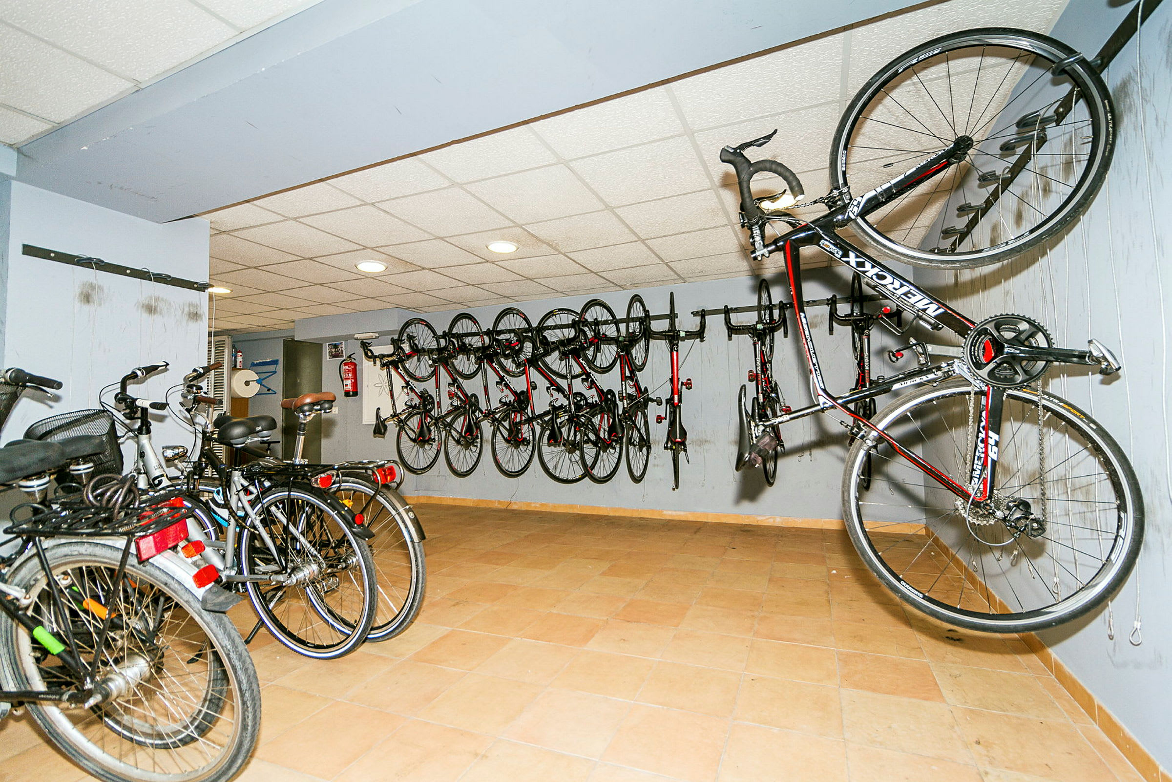 Ett utrymme med cyklar uppställda och en vägg med upphängda cyklar. (AI-genererad text)