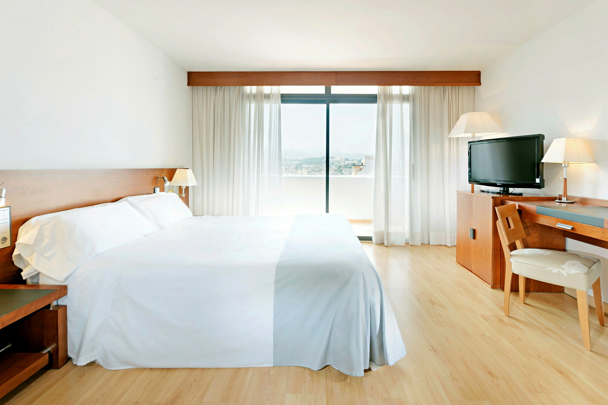 Hotelrum med en stor säng, skrivbord, stol, TV och ett fönster med utsikt. (AI-genererad text)