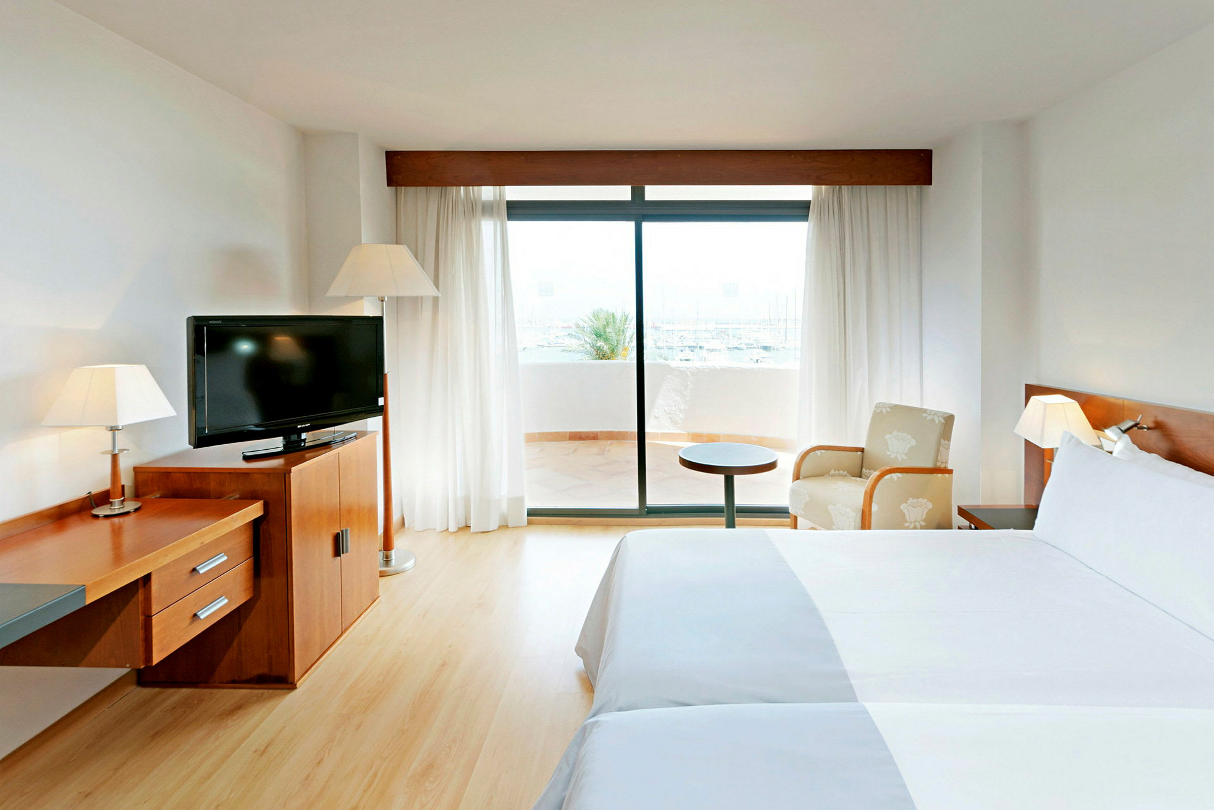 Ett hotellrum med två sängar, en tv på en träbyrå och en glasdörr som leder ut till en terrass. (AI-genererad text)