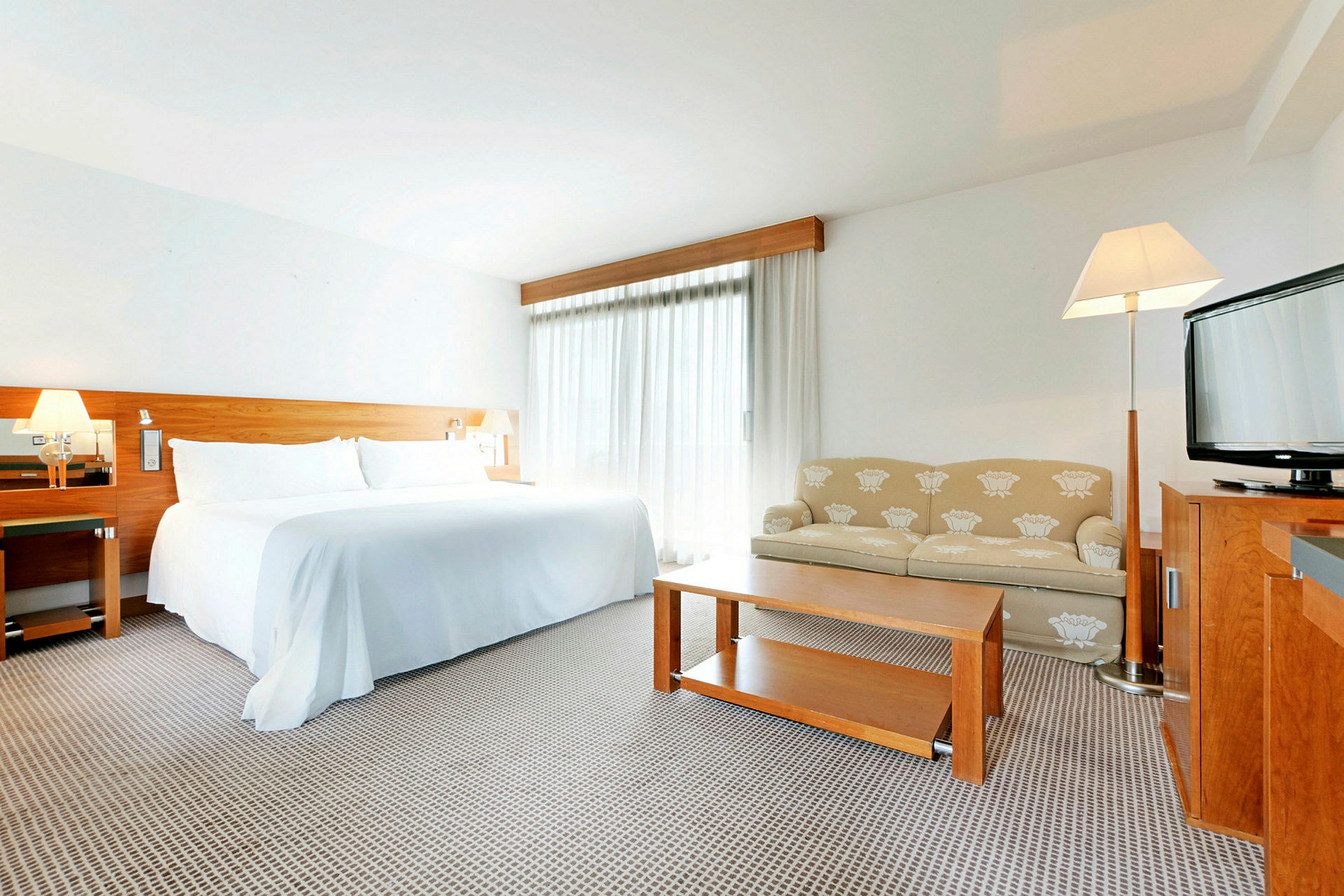 Ett hotellrum med en stor säng, en soffa, ett bord och en TV. Ljus inredning. (AI-genererad text)