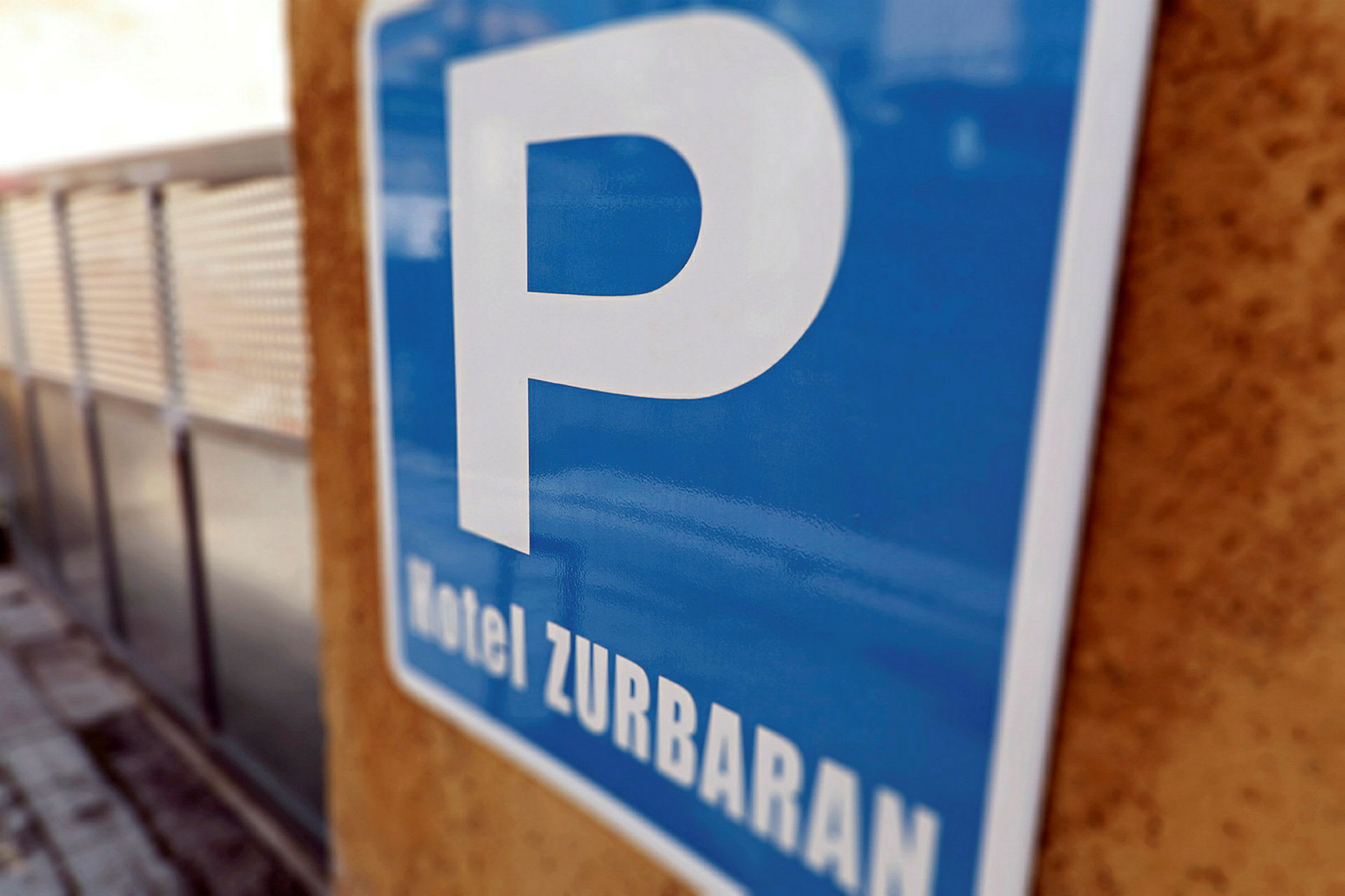 Ett blått parkeringsskylt med texten 'Hotel Zurbaran' som hänger på en vägg. (AI-genererad text)