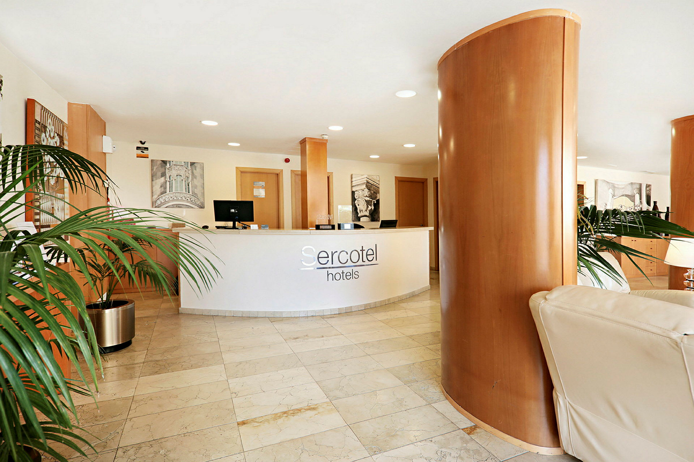Receptionens disk med hotell Sercotel-logotyp syns i en lobby med marmorgolv och dekorativa växter. (AI-genererad text)