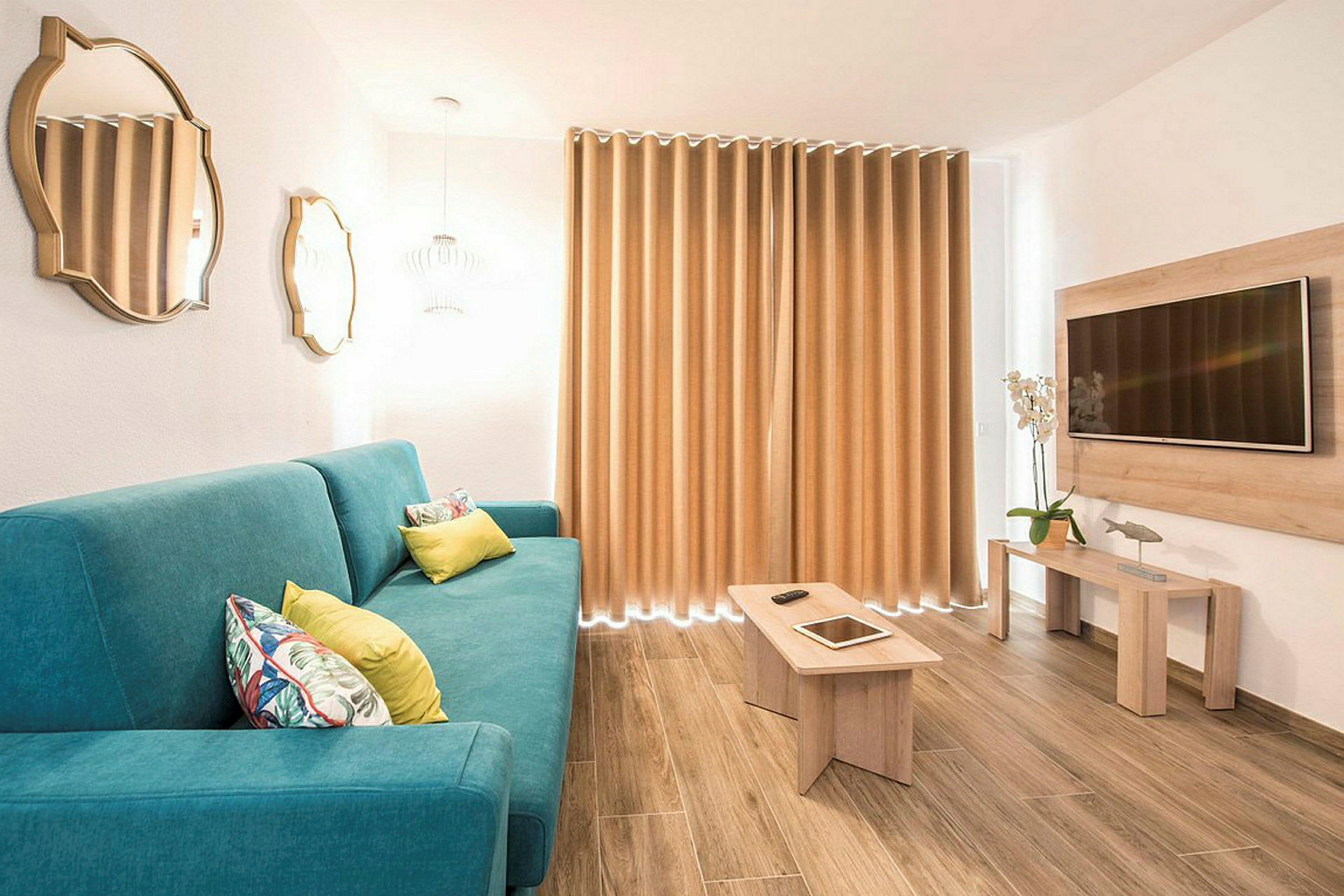 Ett modernt vardagsrum med en blå soffa, träbord, väggmonterad TV och gardiner. (AI-genererad text)