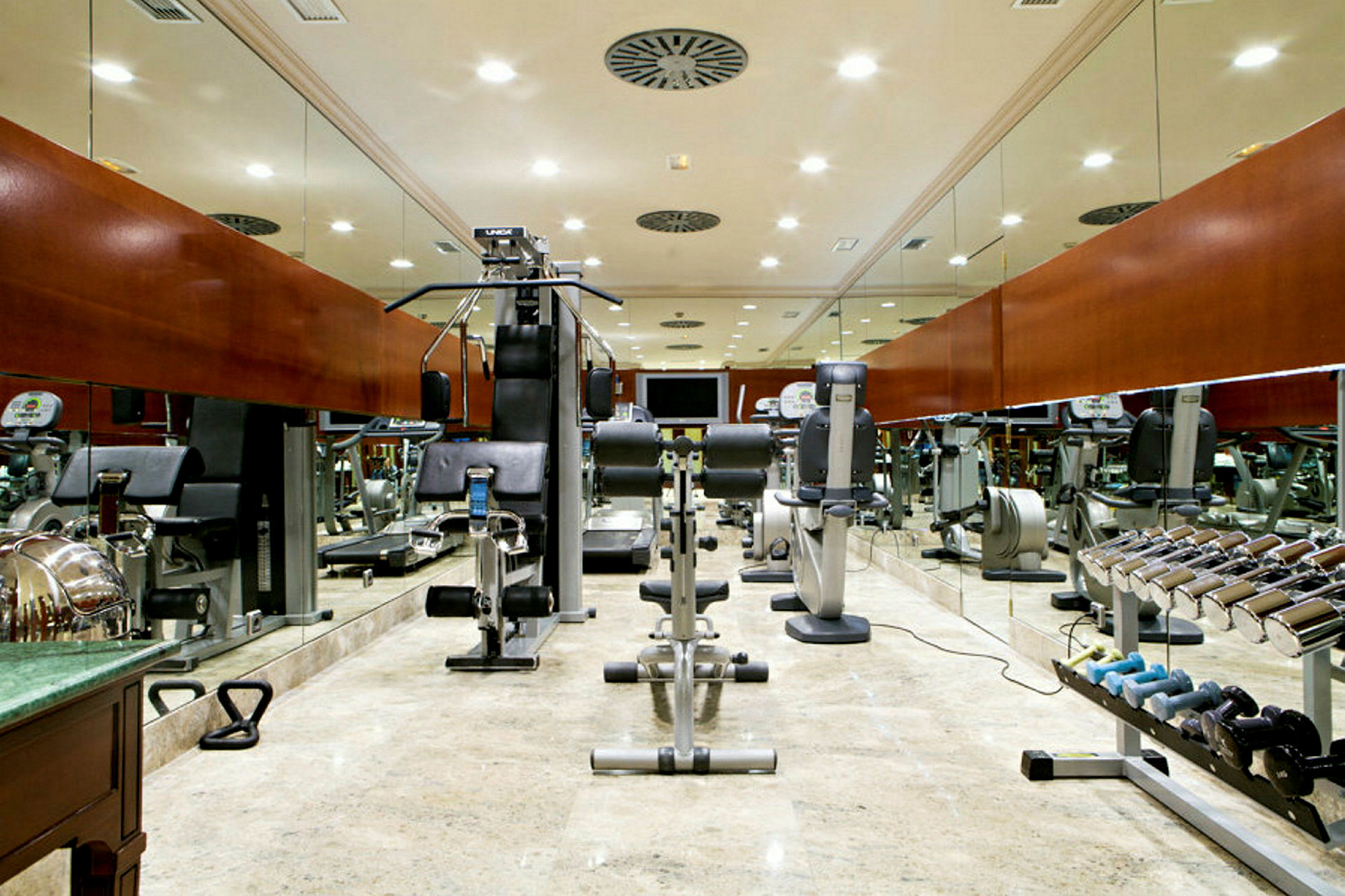 Ett gym med träningsmaskiner och fria vikter, speglar täcker väggarna. (AI-genererad text)