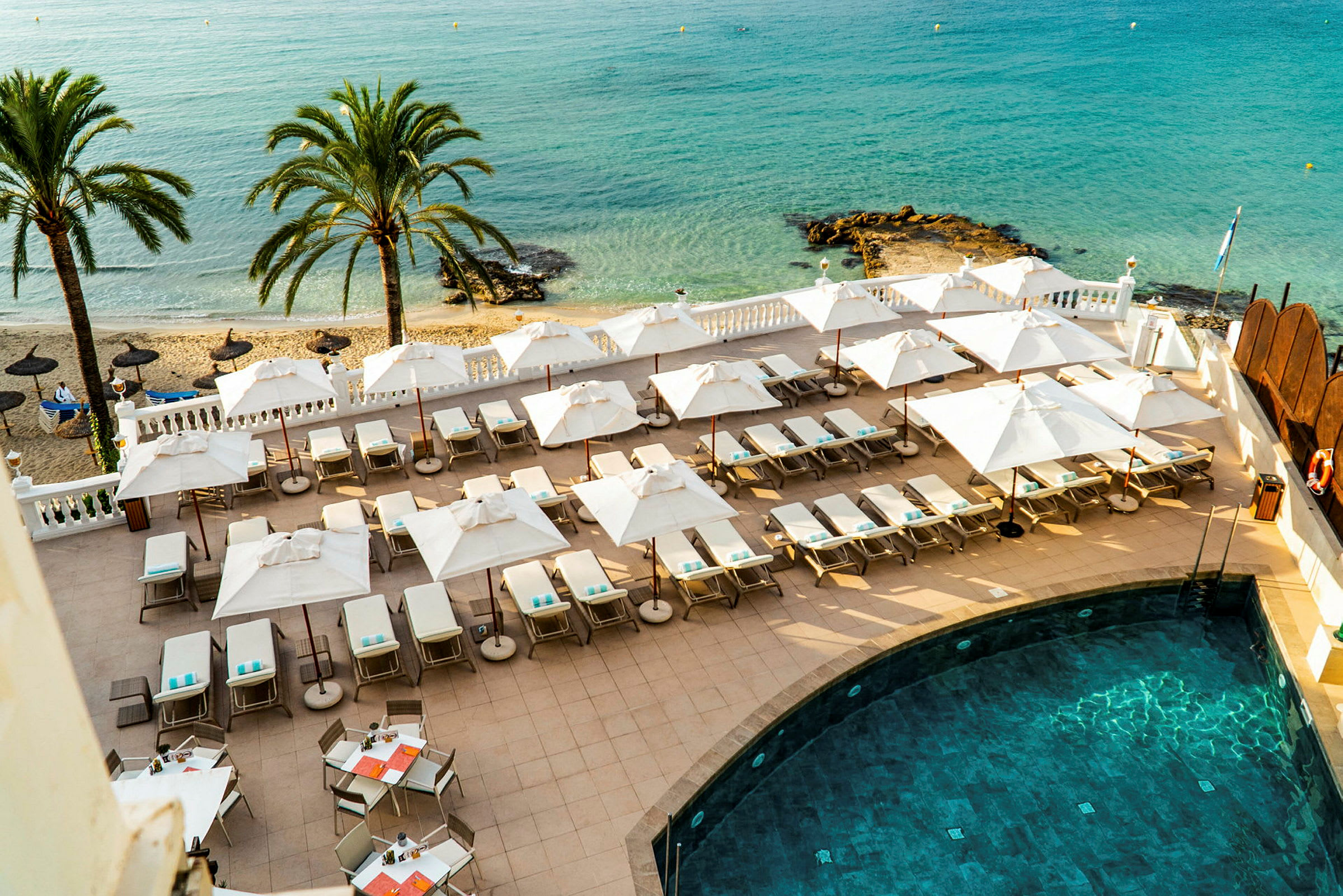 Solstolar och parasoller vid en terrass bredvid en pool med utsikt över stranden och havet. (AI-genererad text)