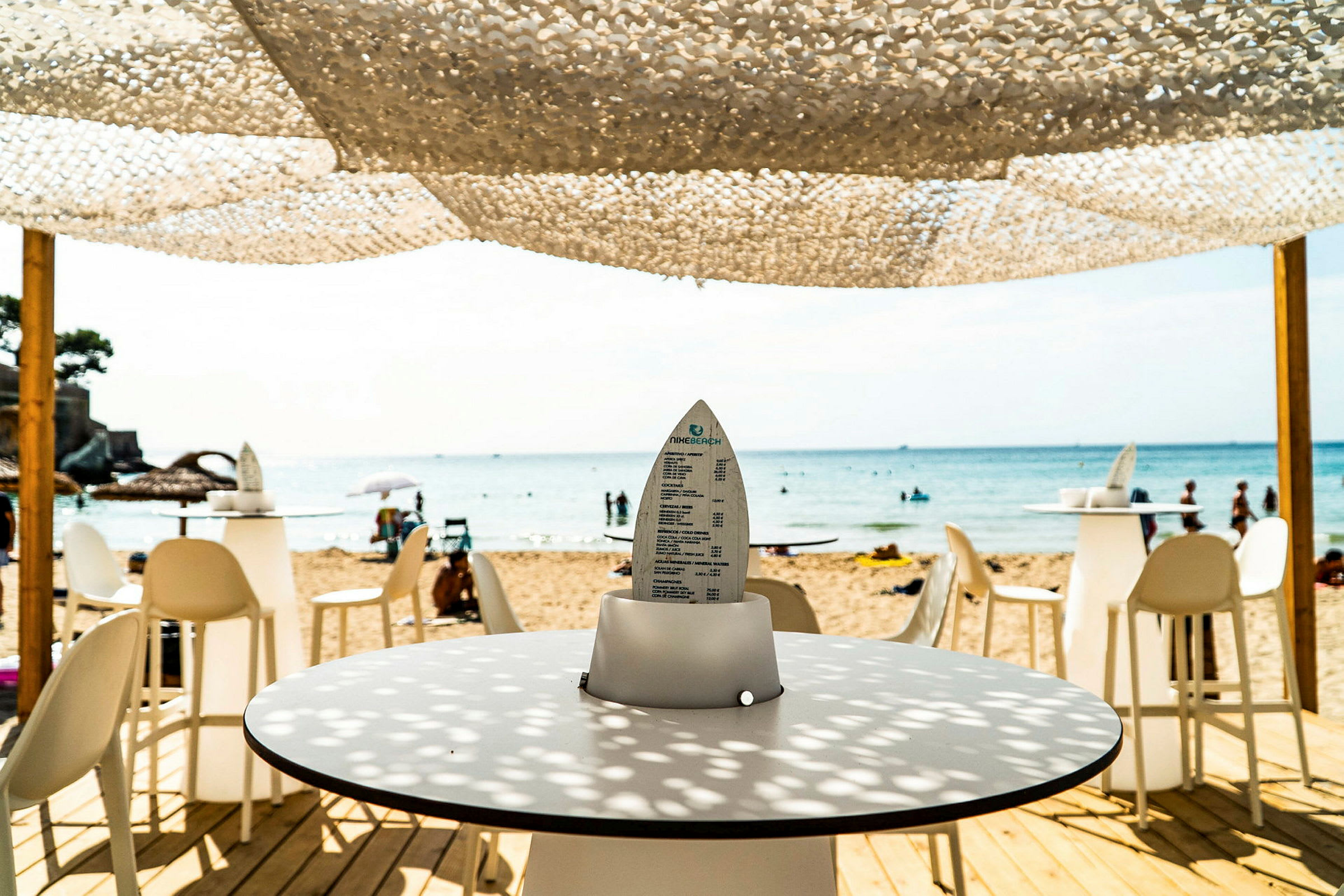 Utsikt från en strandbar mot havet med bord och stolar. (AI-genererad text)