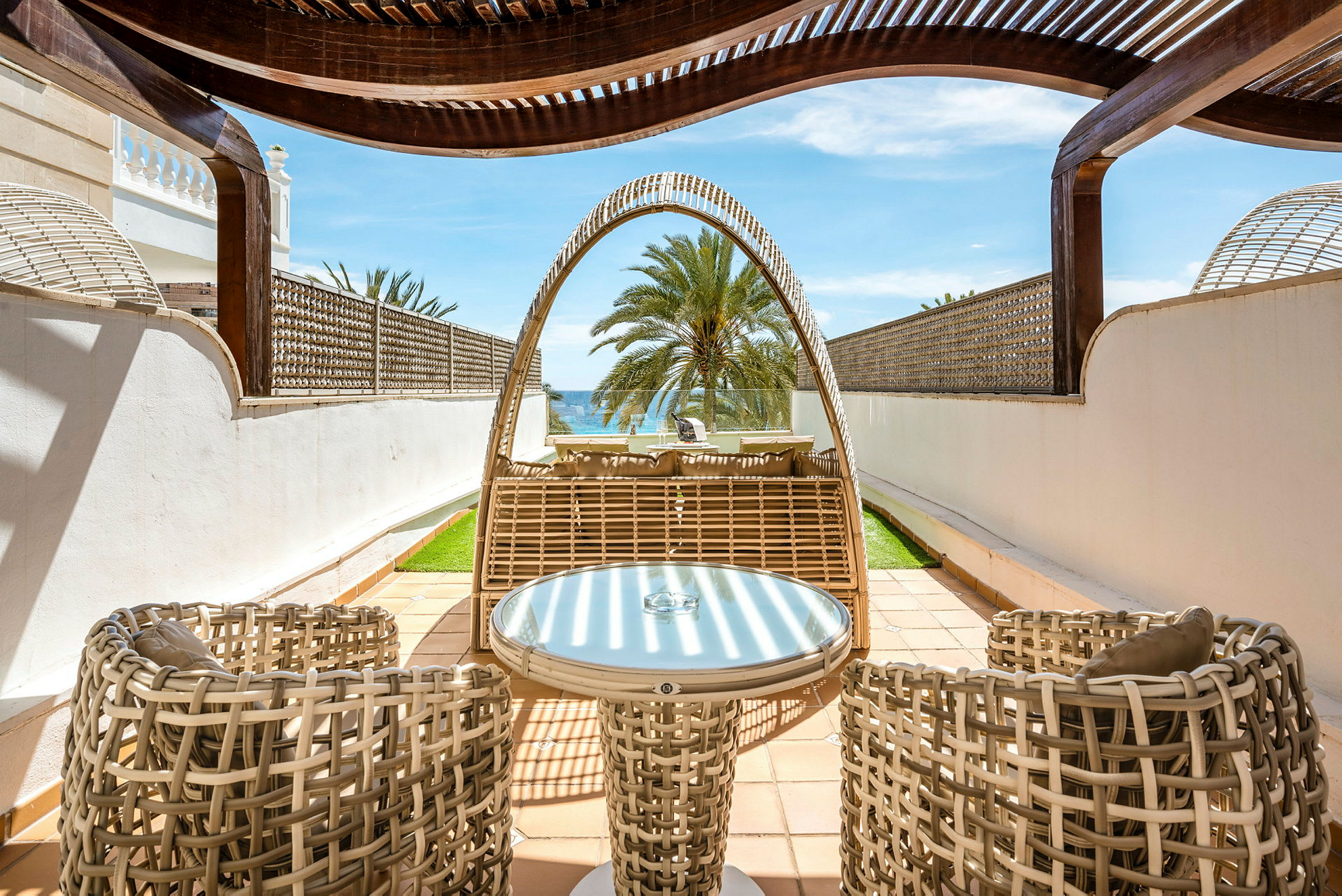 Utemöbler i flätad design på en privat terrass med utsikt över en palm och havet. (AI-genererad text)