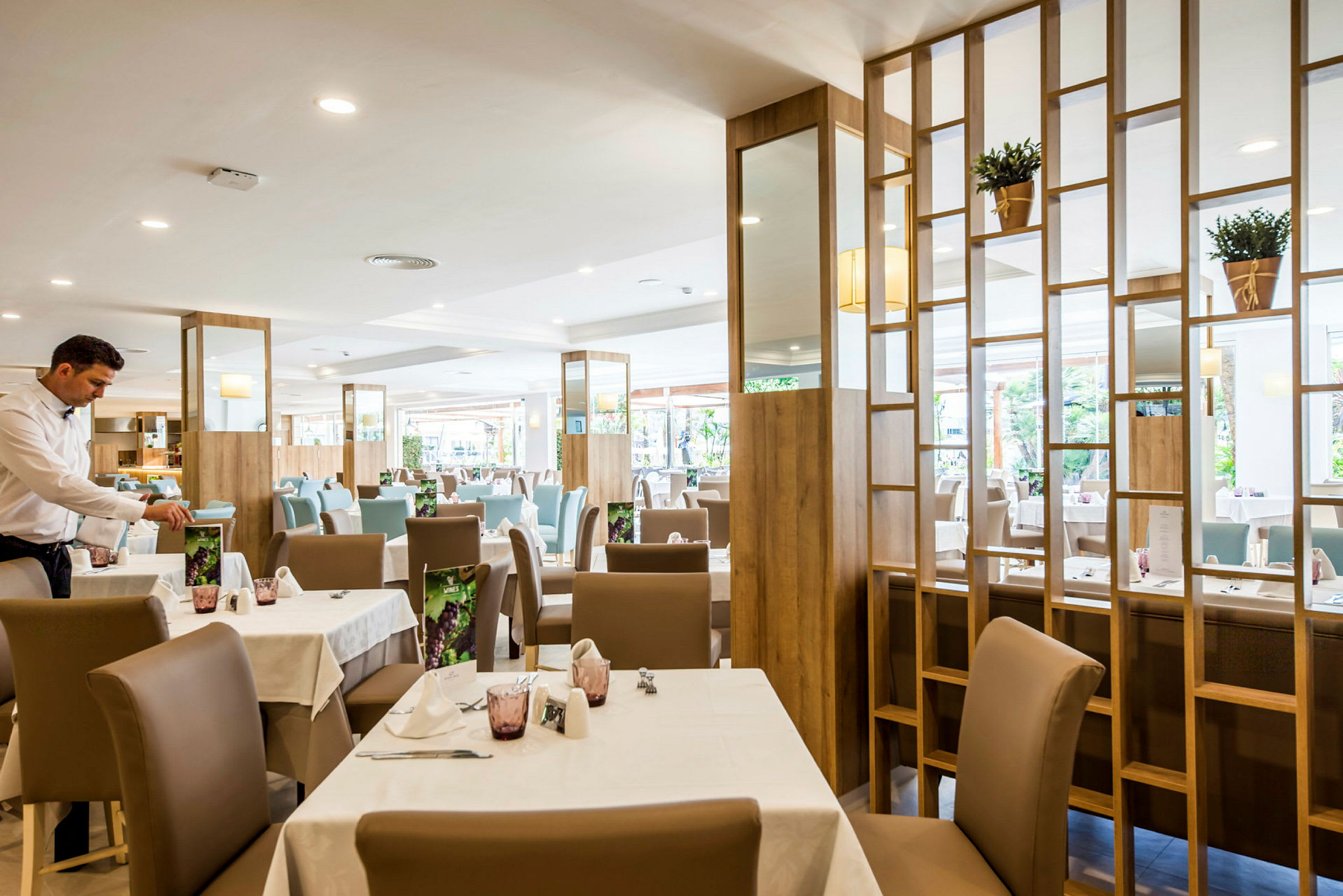 Interiör av en restaurang med dukade bord och en servitör som arbetar. (AI-genererad text)