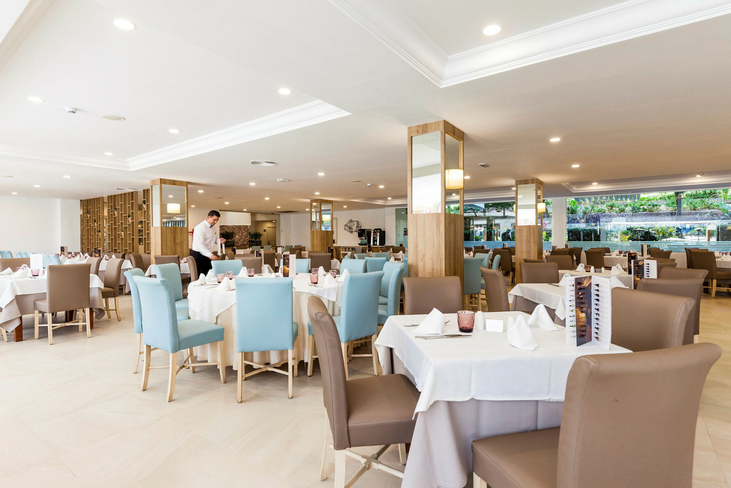 En restaurang med dukade bord och stolar, servitör som arbetar. (AI-genererad text)