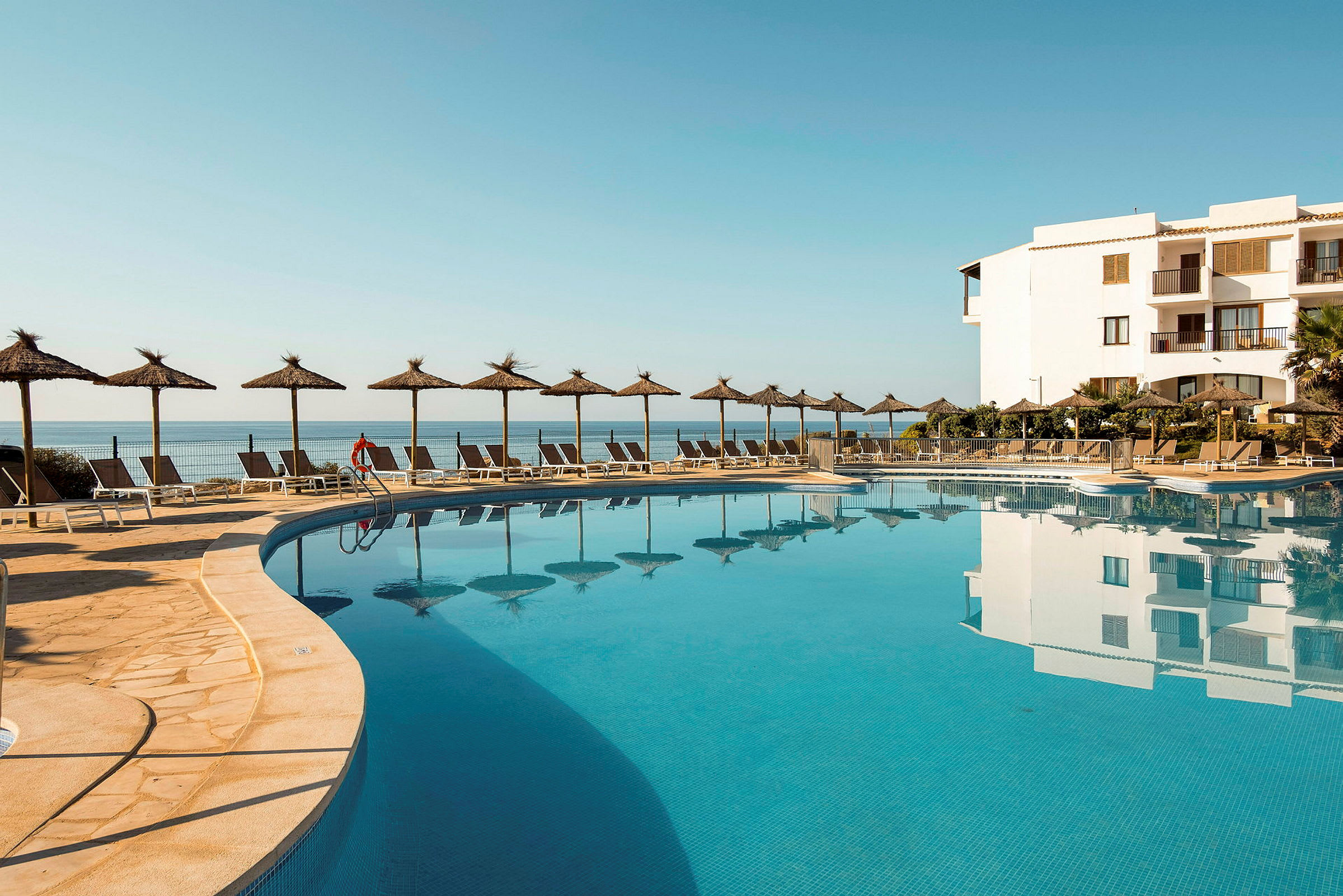 En utomhuspool vid ett hotell med parasoller och solstolar, havet i bakgrunden. (AI-genererad text)