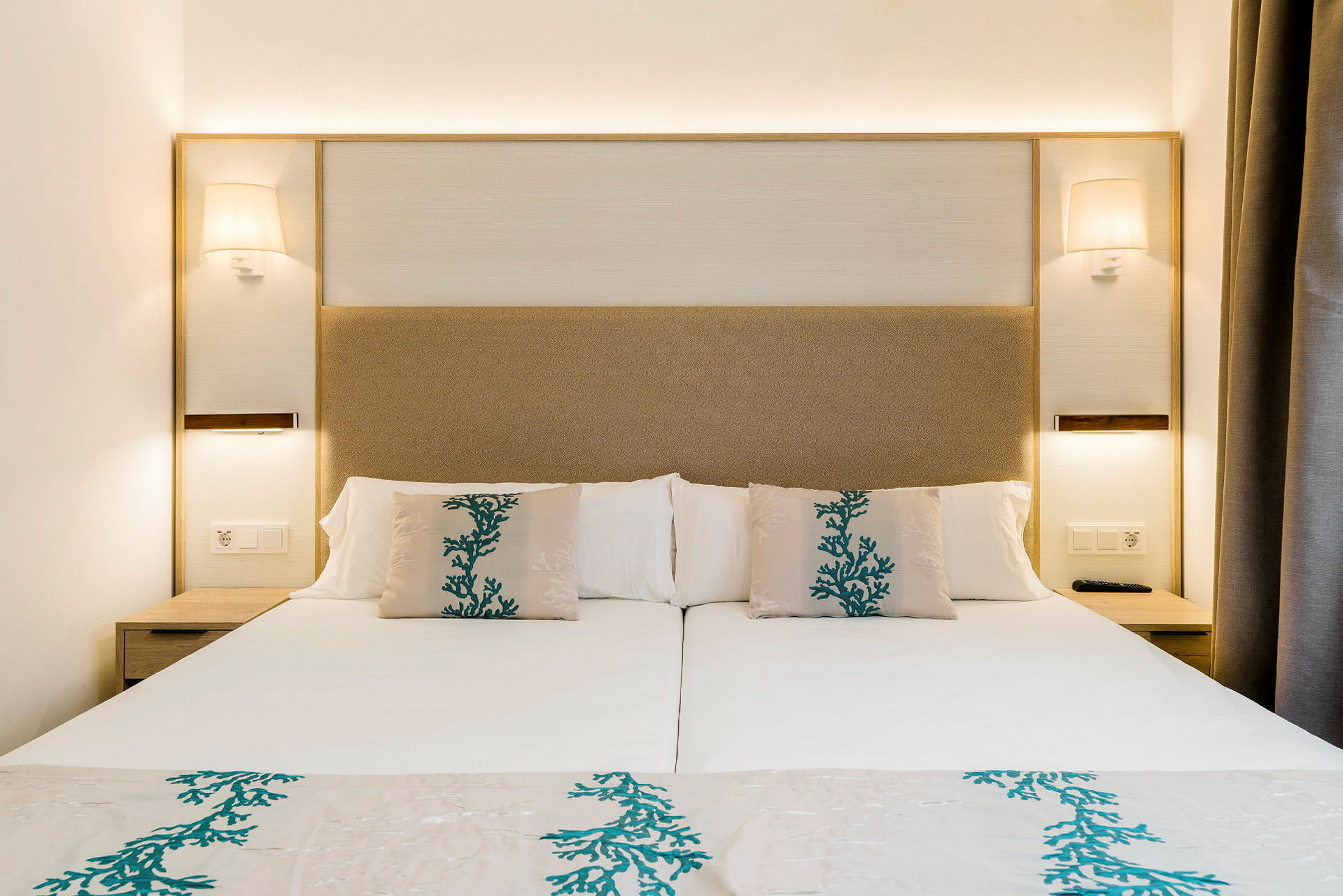 En hotellrumsäng med vita sängkläder och kuddar dekorerade med blågrönt mönster. (AI-genererad text)