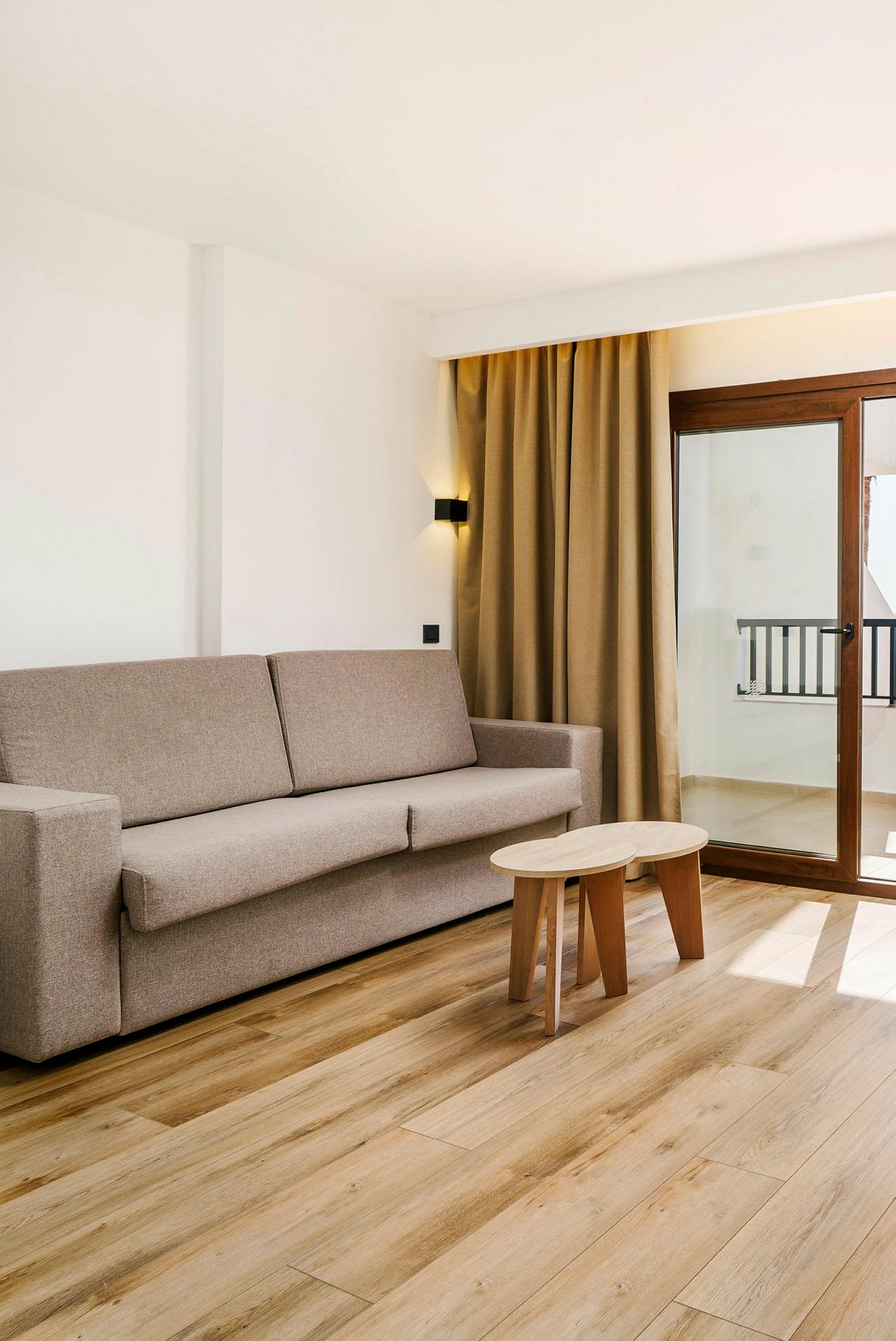 Ett vardagsrum med en beige soffa, ett träbord och stora fönster med gardiner. (AI-genererad text)