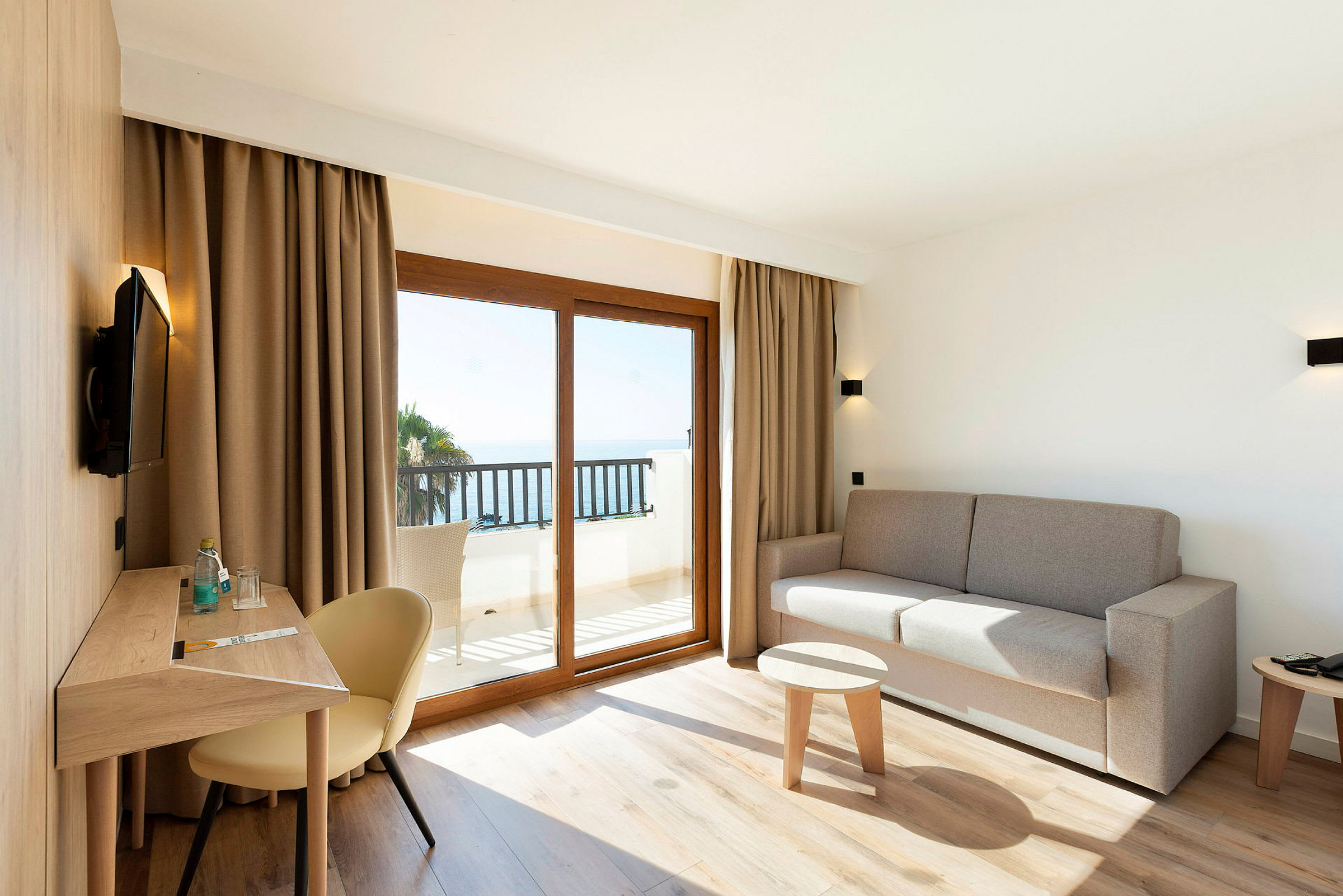 Modernt möblerat hotellrum med sittgrupp och utsikt mot havet. (AI-genererad text)