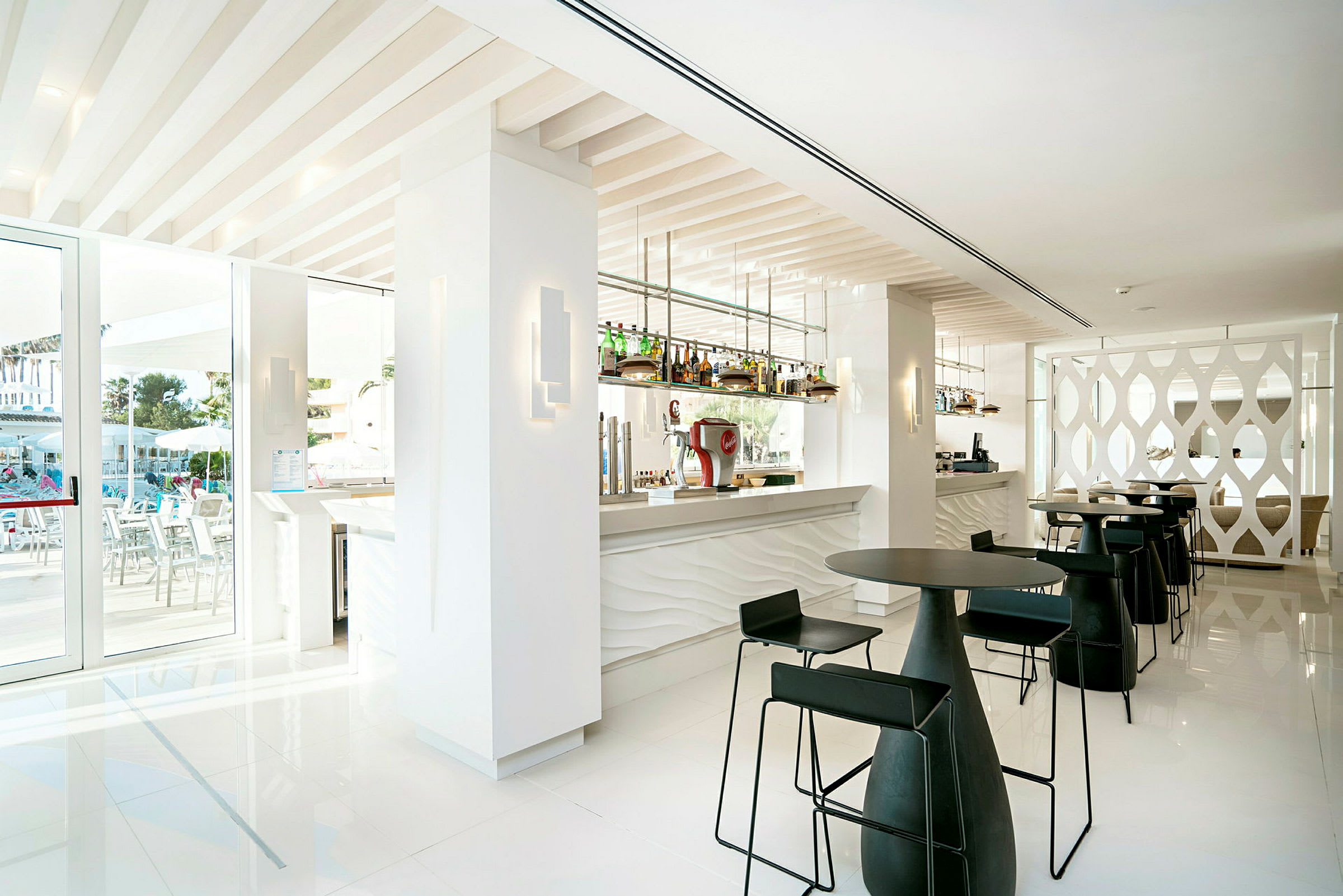 Ett modernt hotellbarområde med vita väggar, svarta stolar och en rad flaskor vid bardisken. (AI-genererad text)