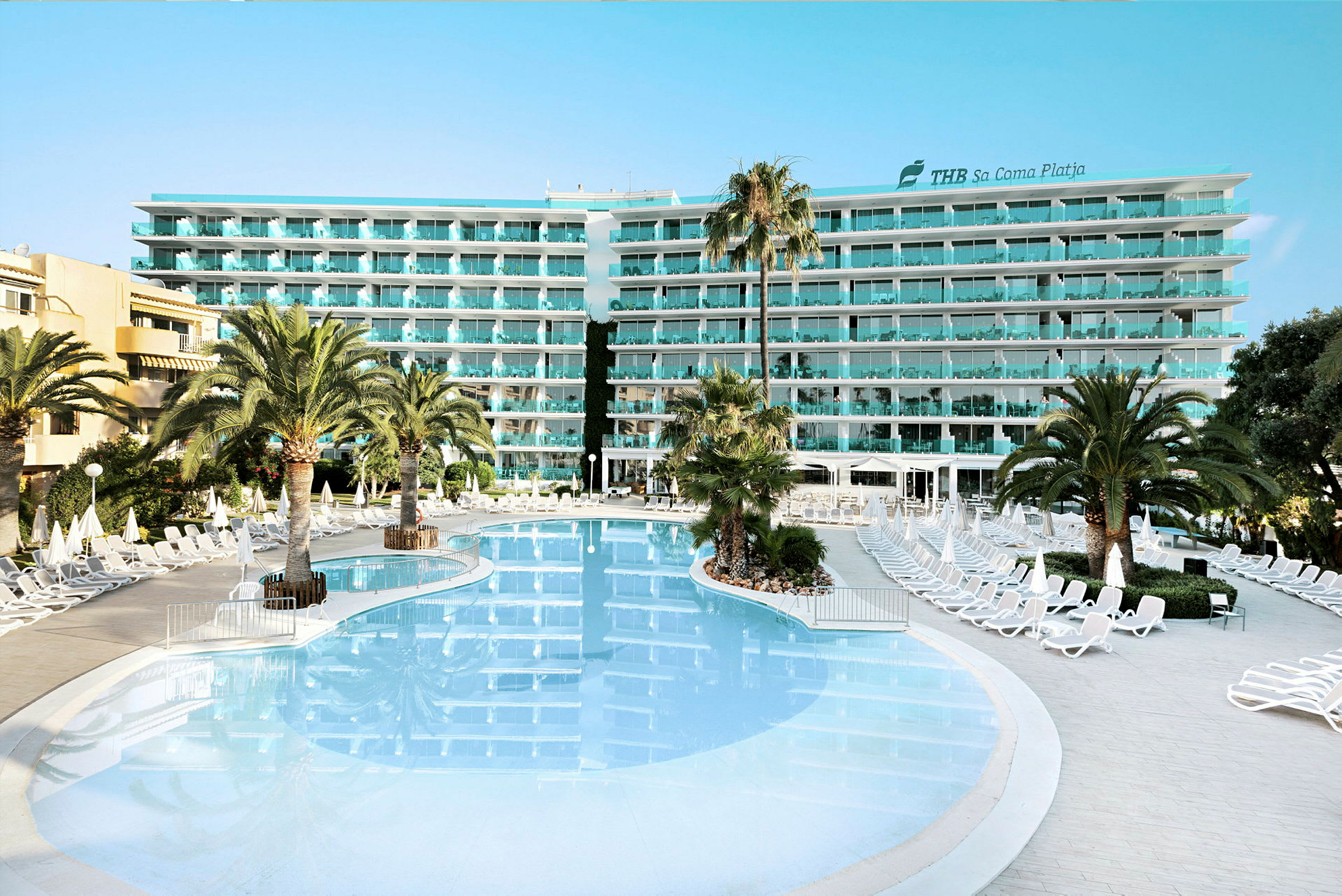 Hotellbyggnad med flera våningar sedd bakom en stor pool och solstolar. (AI-genererad text)