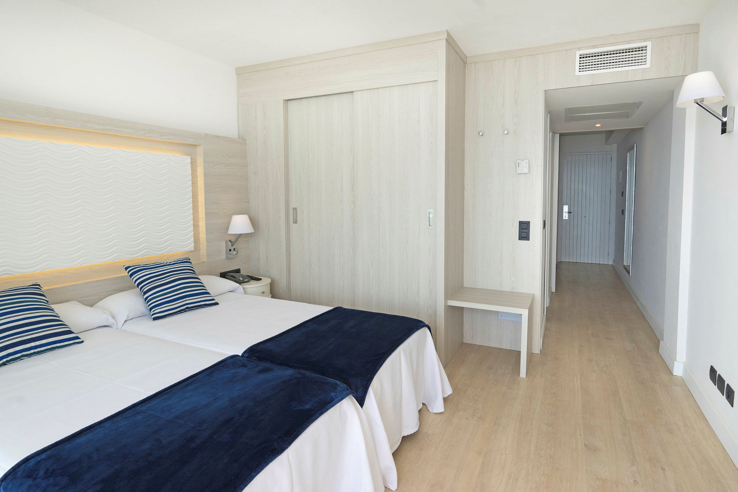 Ett hotellrum med två enkelsängar, blå-randiga kuddar och mörkblå filtar. (AI-genererad text)