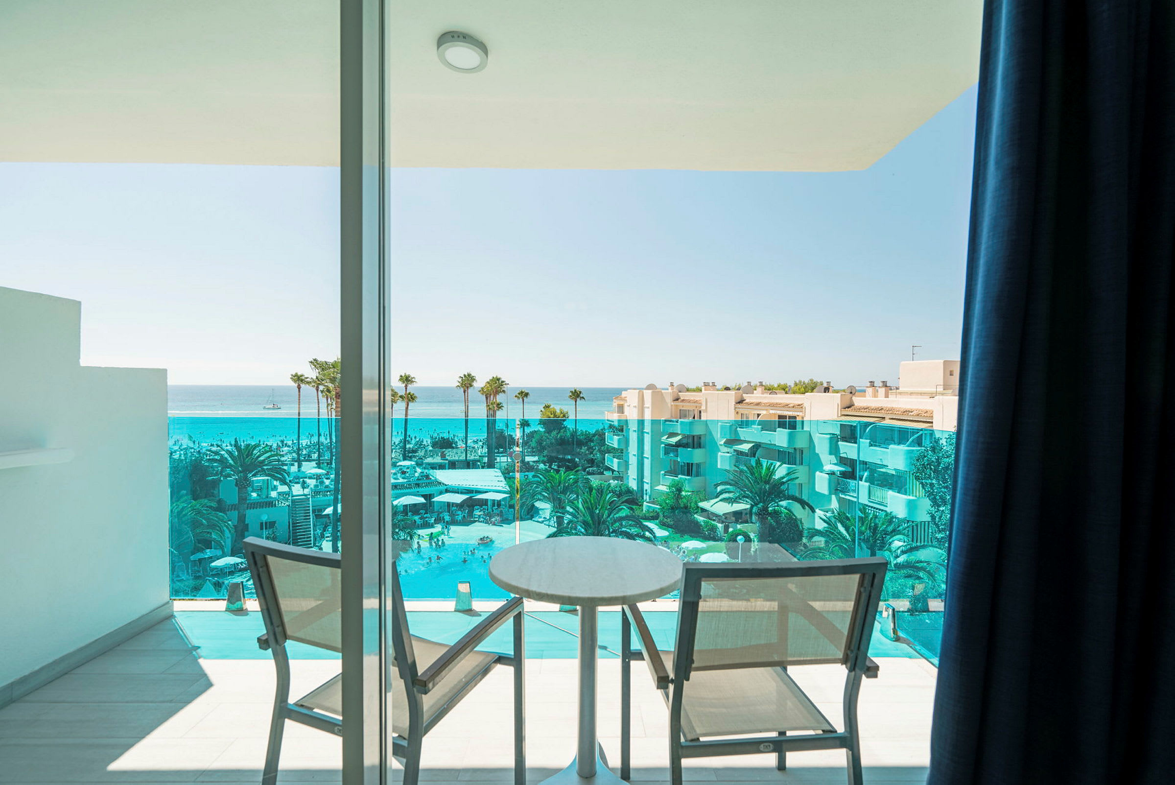 Utsikt från en balkong med två stolar och ett bord mot havet och en hotellpool. (AI-genererad text)