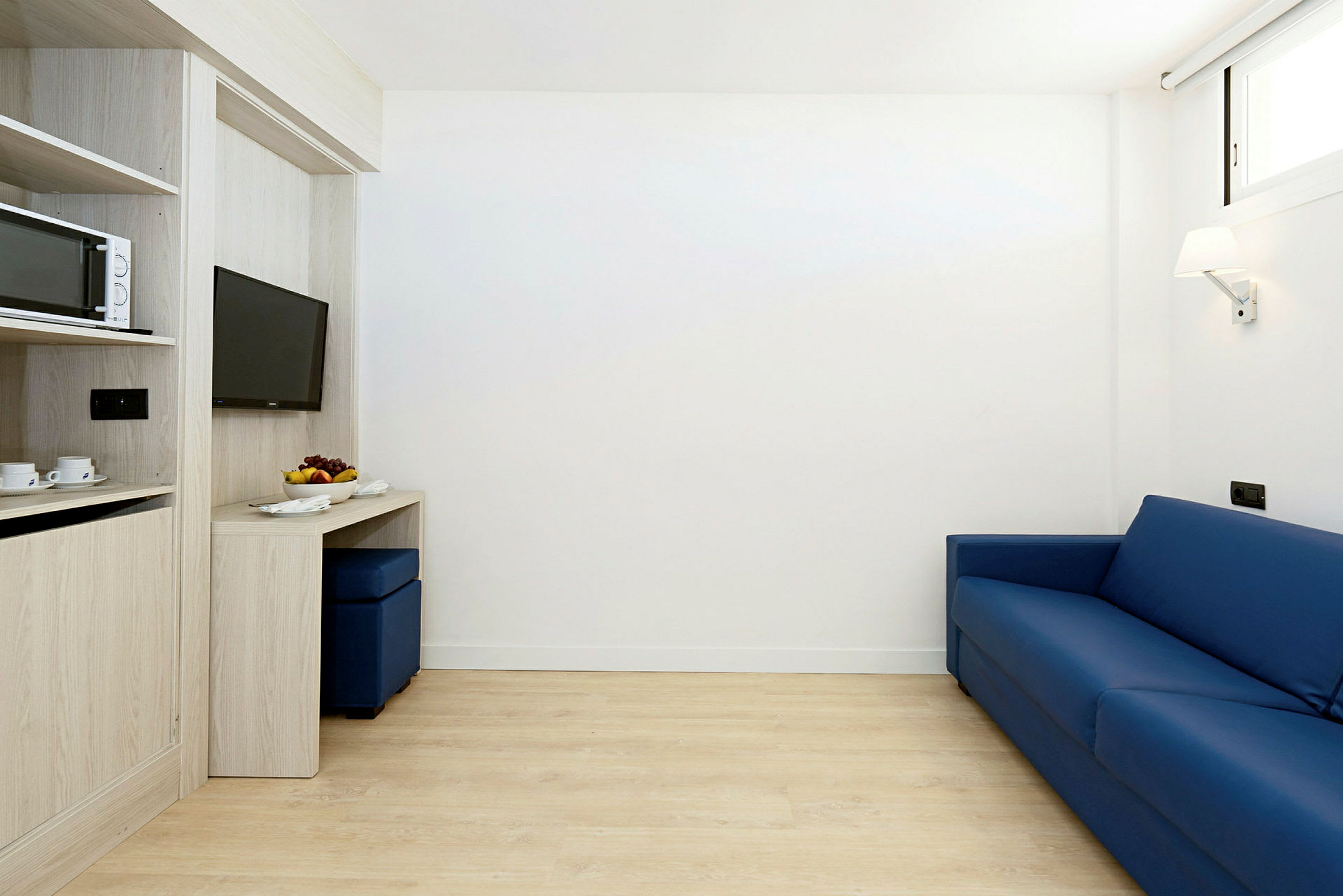 Ett rum med en blå soffa, ett arbetsbord och en vägghängd TV. (AI-genererad text)