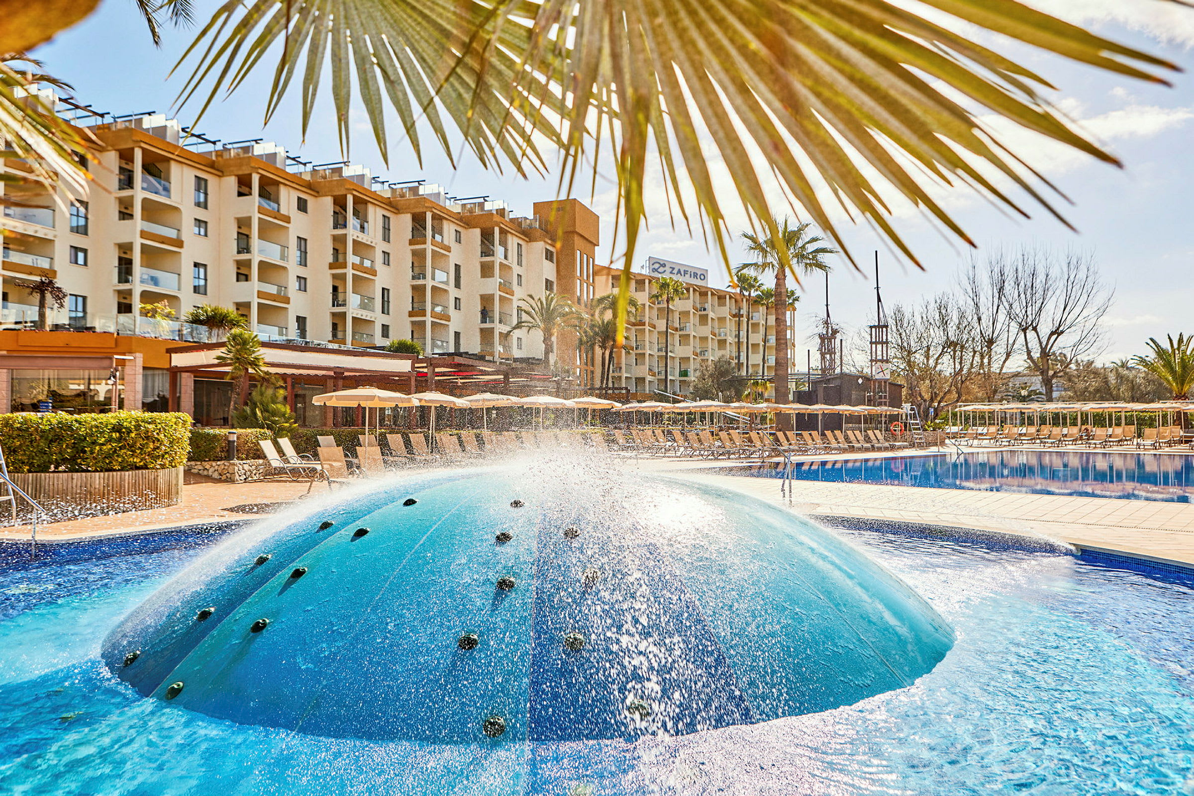 Hotellets poolområde med solstolar och en fontän. (AI-genererad text)