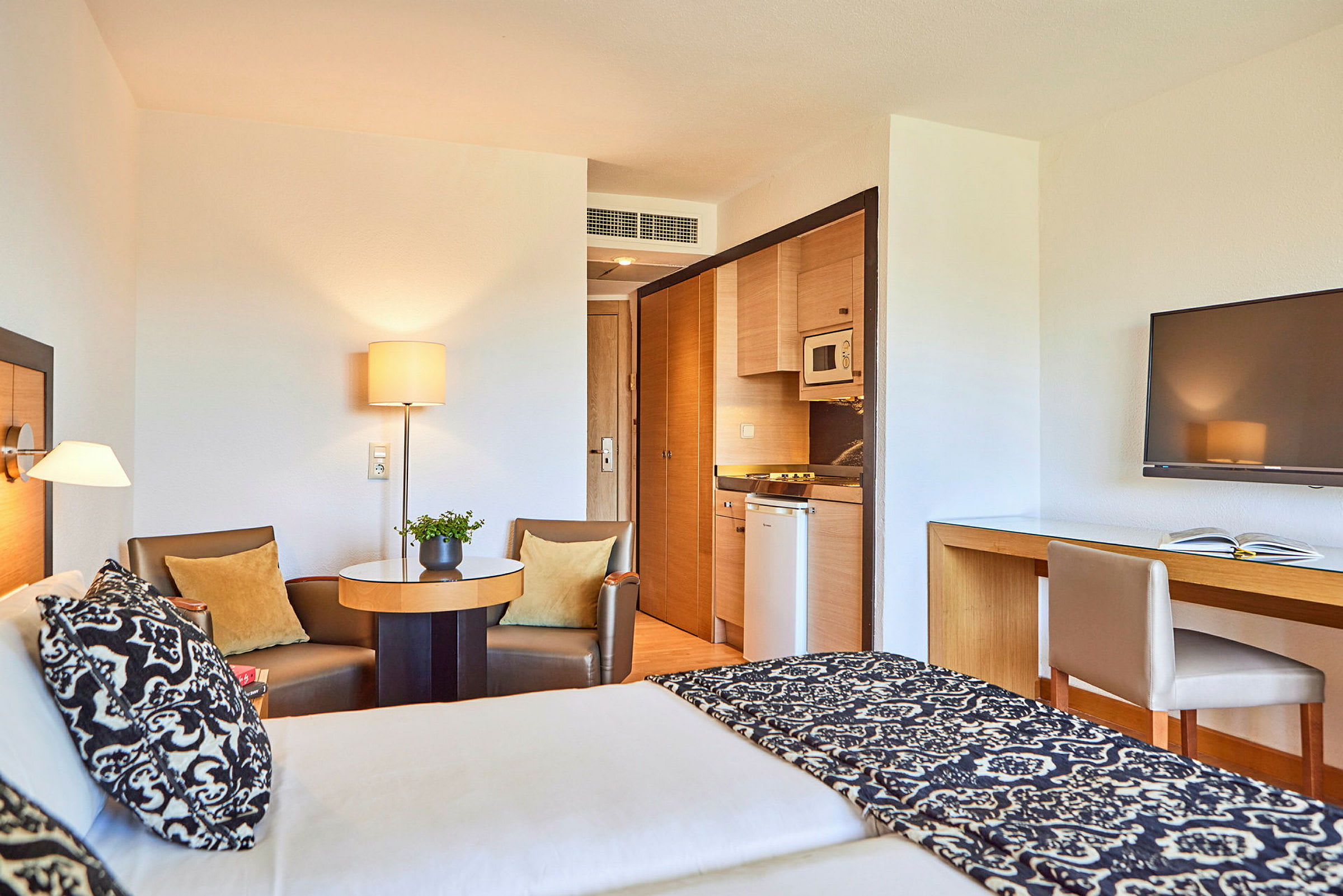 Hotellrum med en dubbelsäng, sittgrupp, kök samt skrivbord med TV. (AI-genererad text)