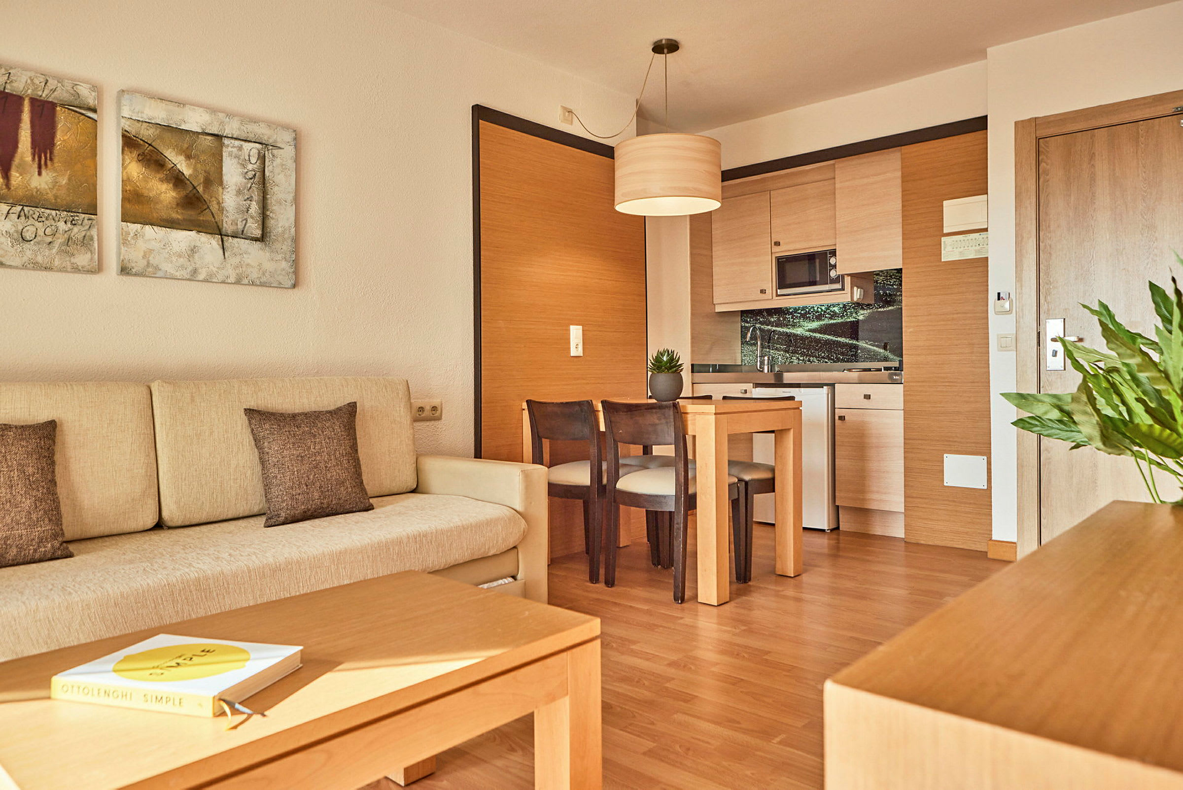 Foto av ett modernt hotellrum med en ljus soffa, ett träbord med stolar och ett hörnkök. (AI-genererad text)