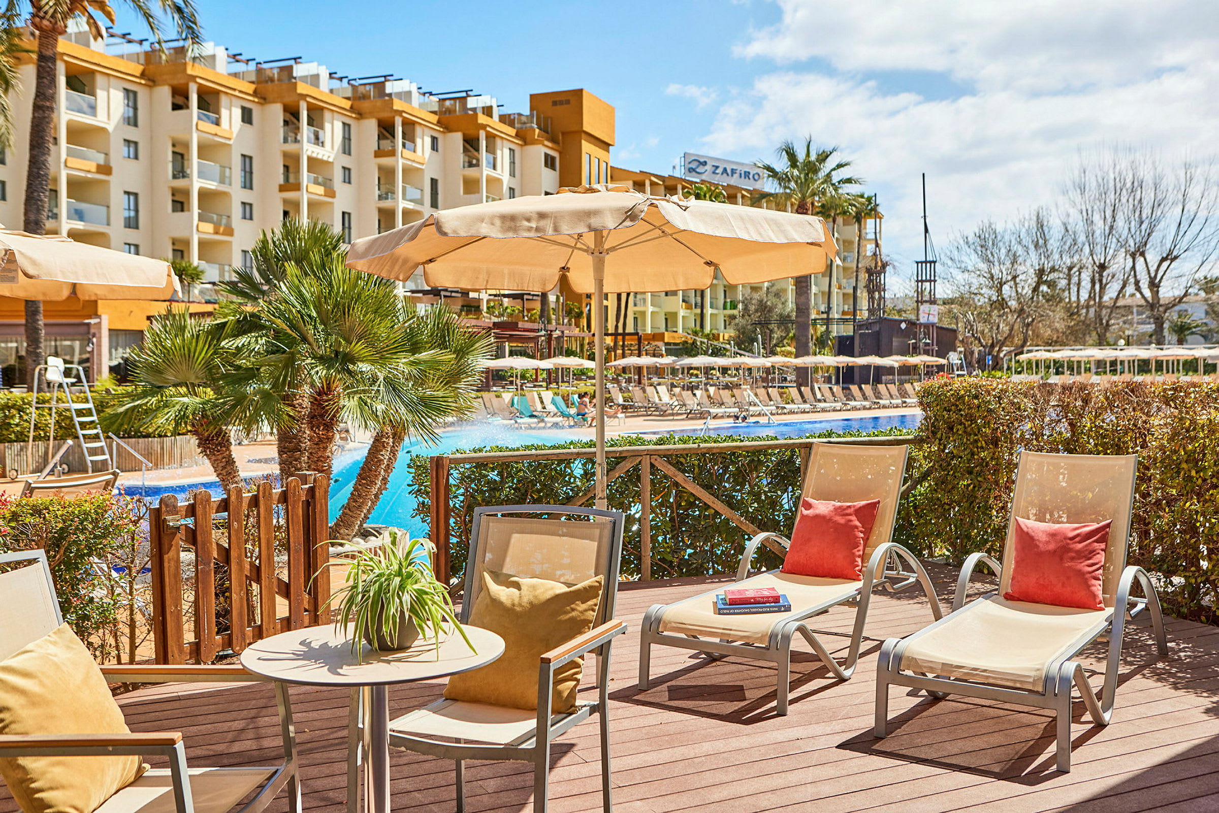 Utemiljö vid pool med solstolar och parasoller, hotellbyggnad i bakgrunden. (AI-genererad text)