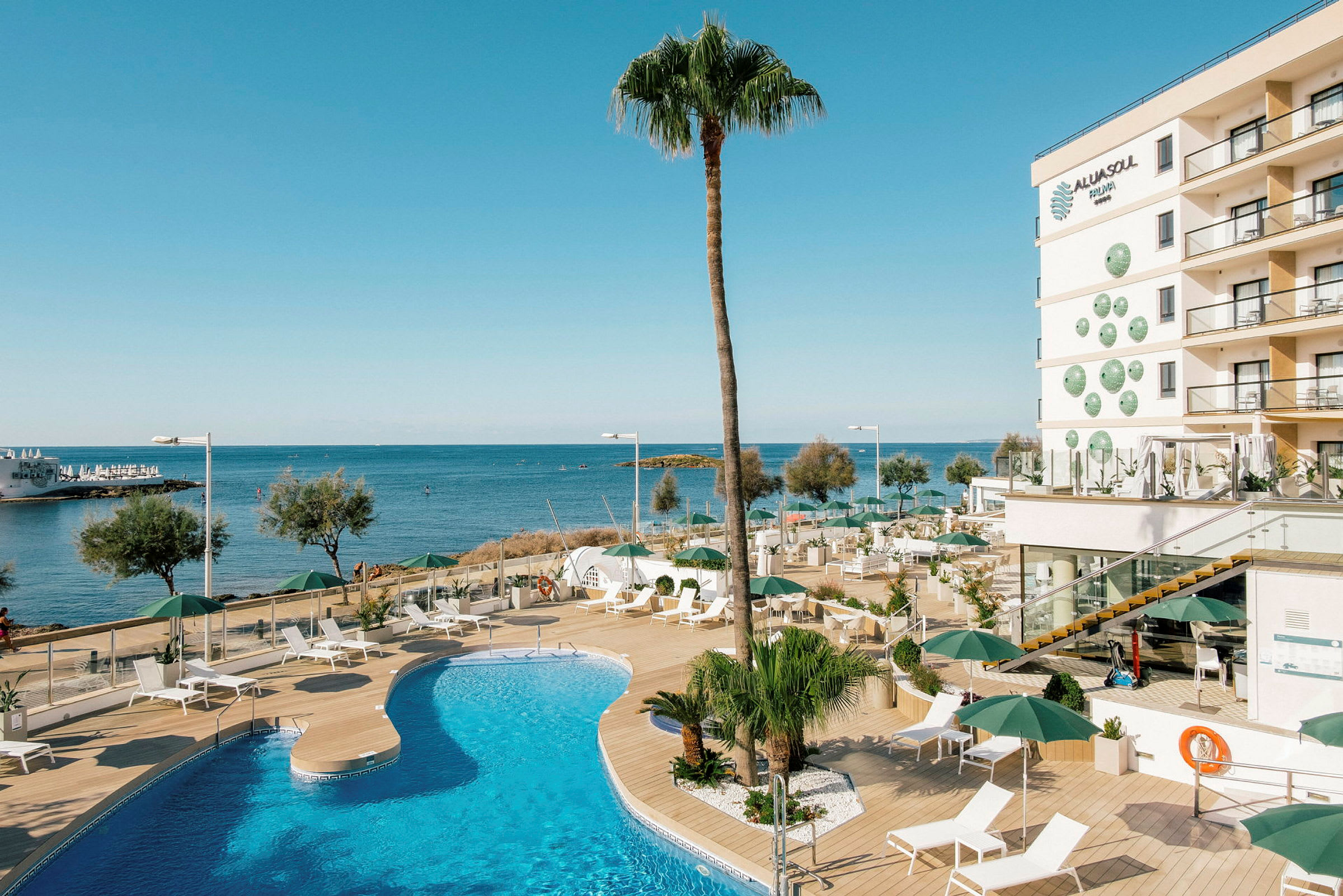En utomhuspool vid ett hotell nära havet med solstolar och parasoller på en träterrass. (AI-genererad text)