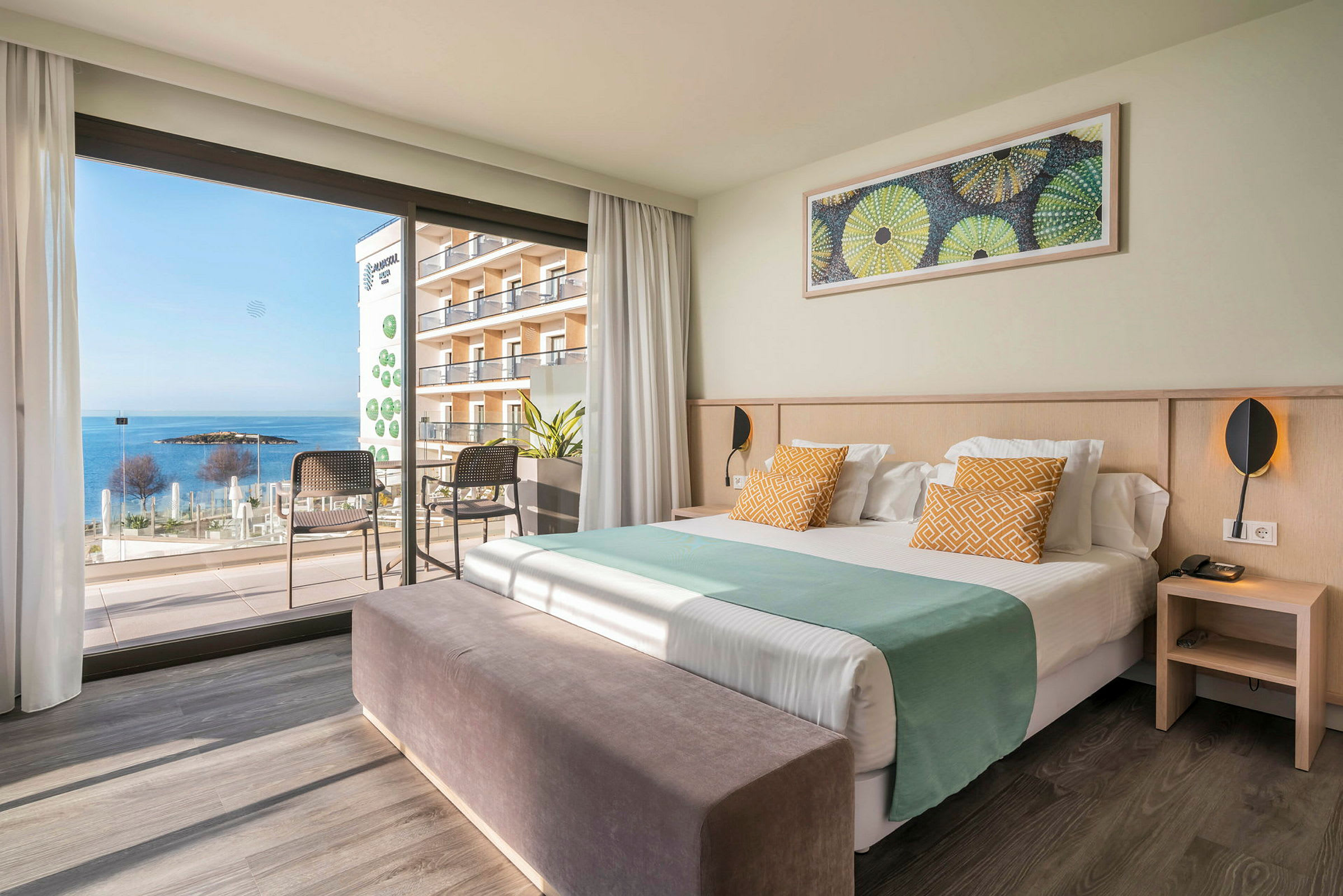 Hotellrum med säng, sittmöbler och en utsikt mot havet genom stora fönster. (AI-genererad text)