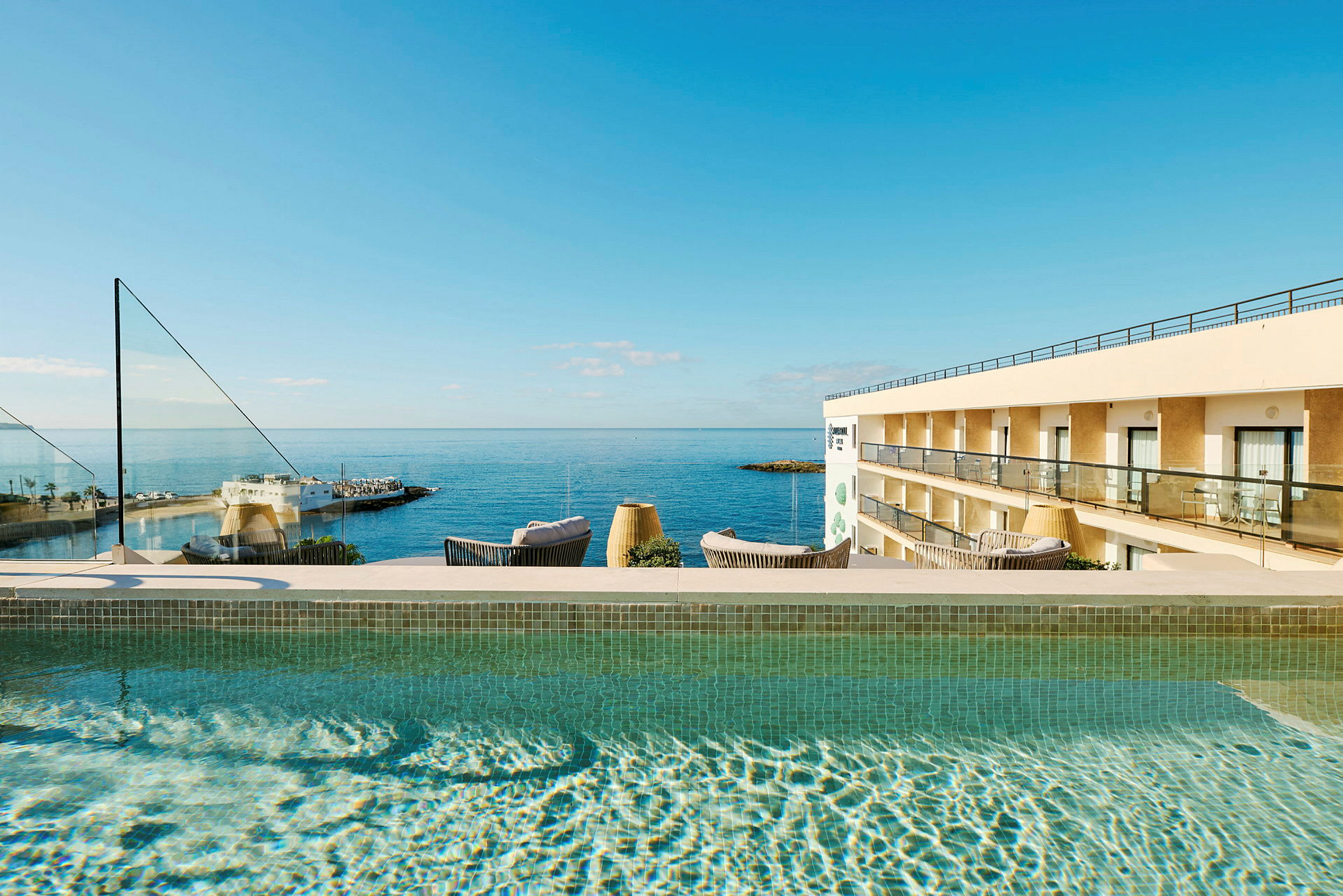 Utomhuspool med utsikt över havet och en hotellbyggnad. (AI-genererad text)