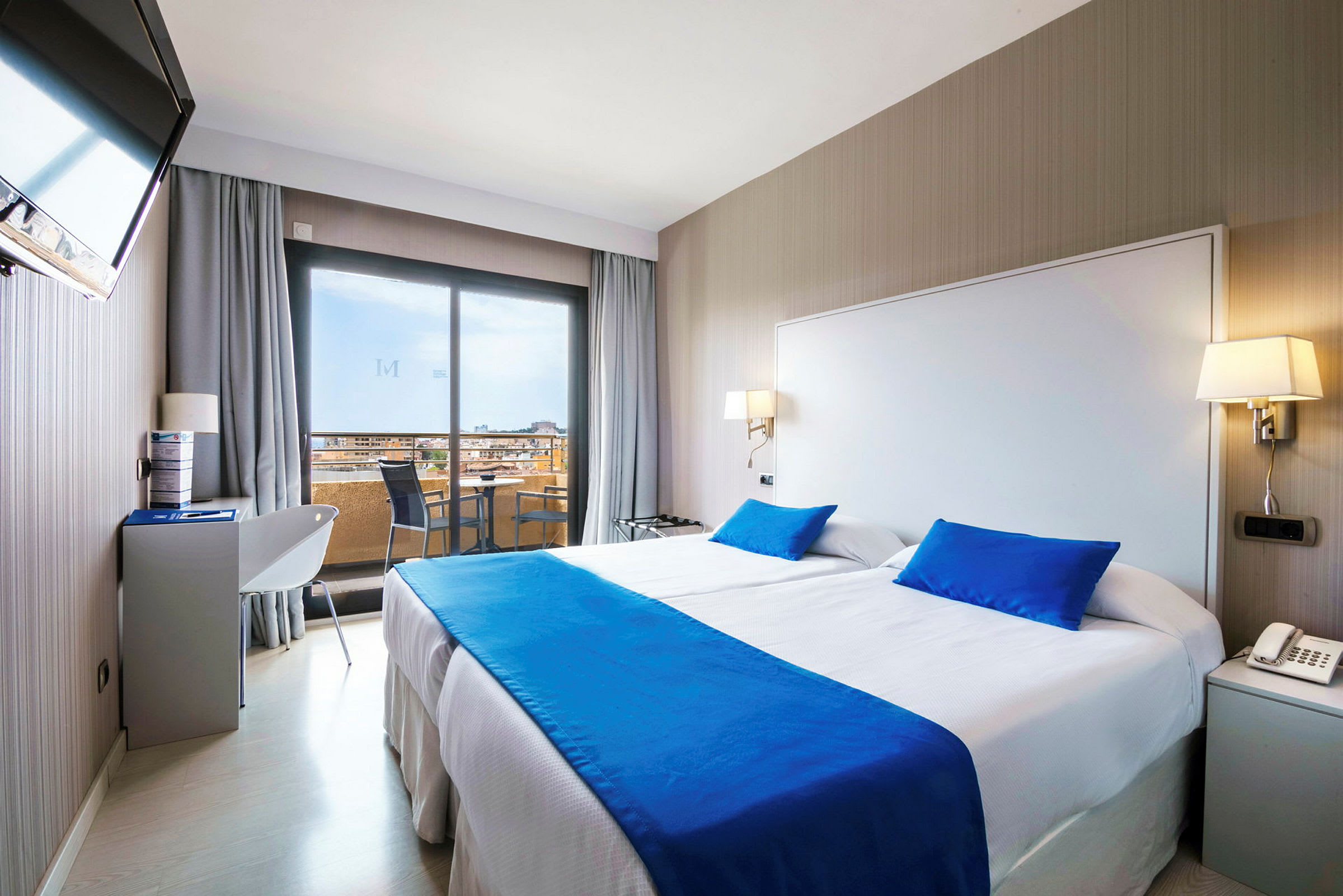 Ett hotellrum med en dubbelsäng, ljusa väggar och blå sängkläder. (AI-genererad text)
