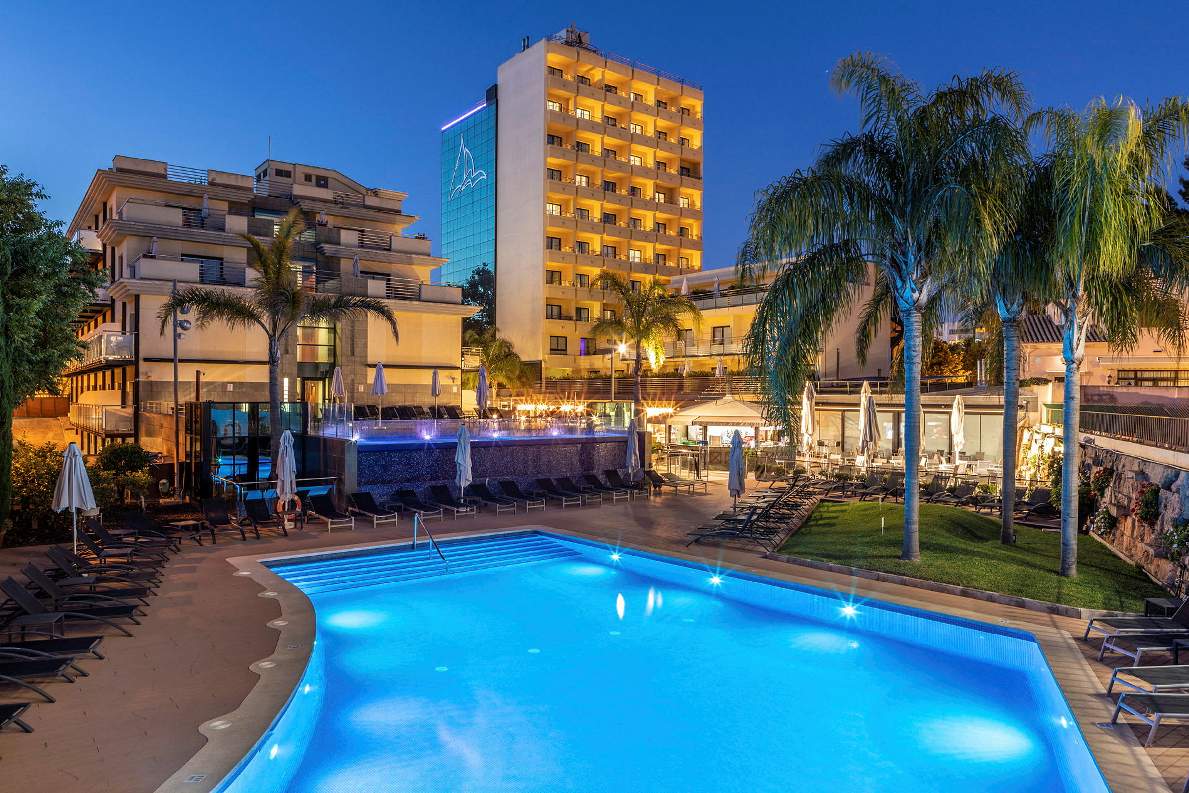Ett hotellområde på kvällen med pool, stolar och belysning. (AI-genererad text)