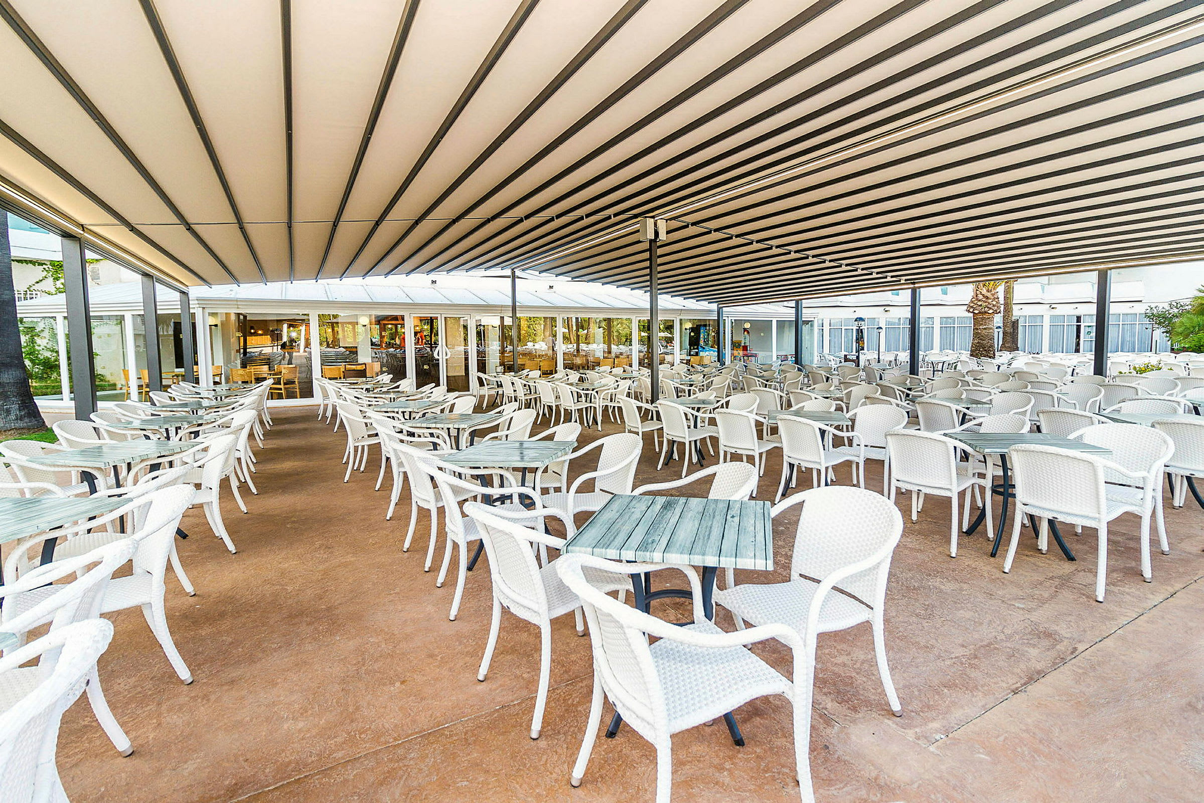 En utomhusrestaurang med många vita bord och stolar under ett tak. (AI-genererad text)