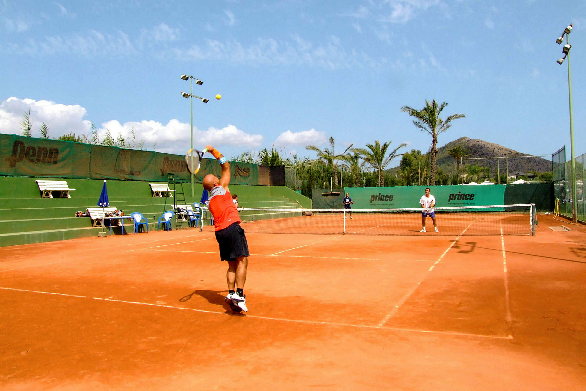 Två personer spelar tennis på en grusplan utomhus under en solig dag. (AI-genererad text)
