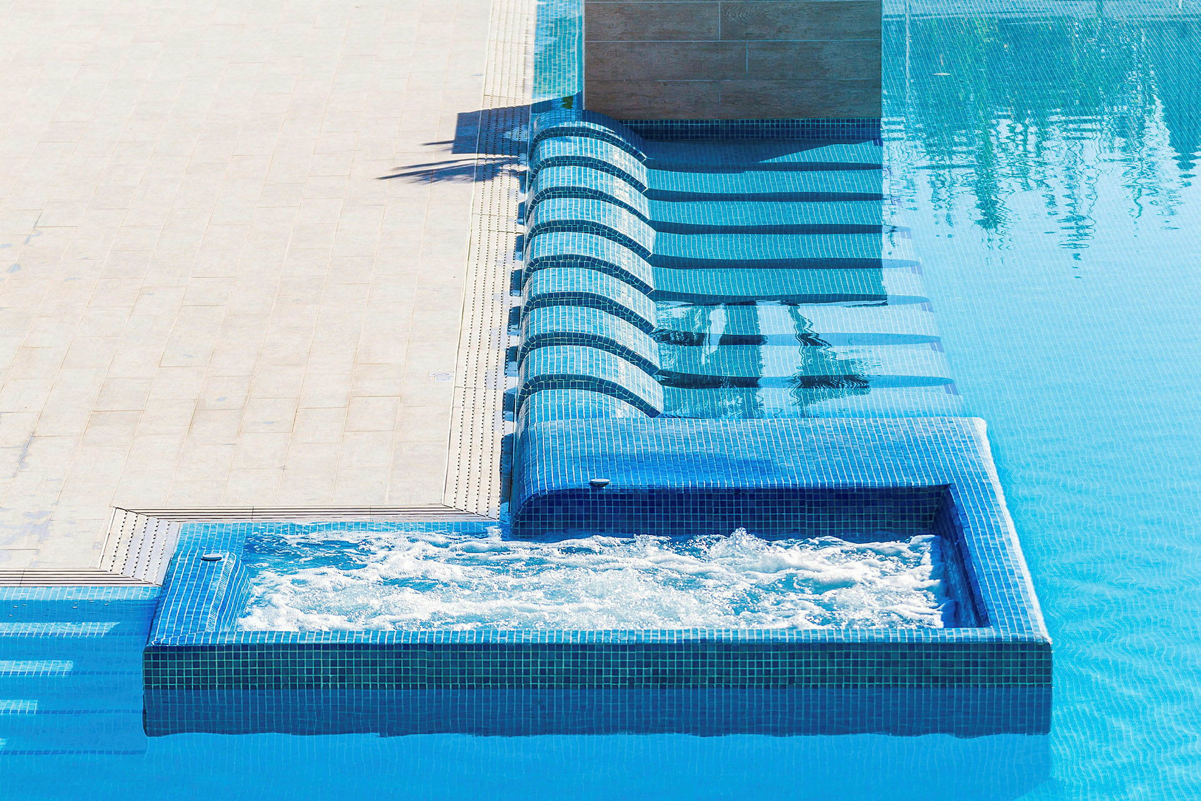 En swimmingpool med blå mosaikplattor och en separat bubbelpool. (AI-genererad text)