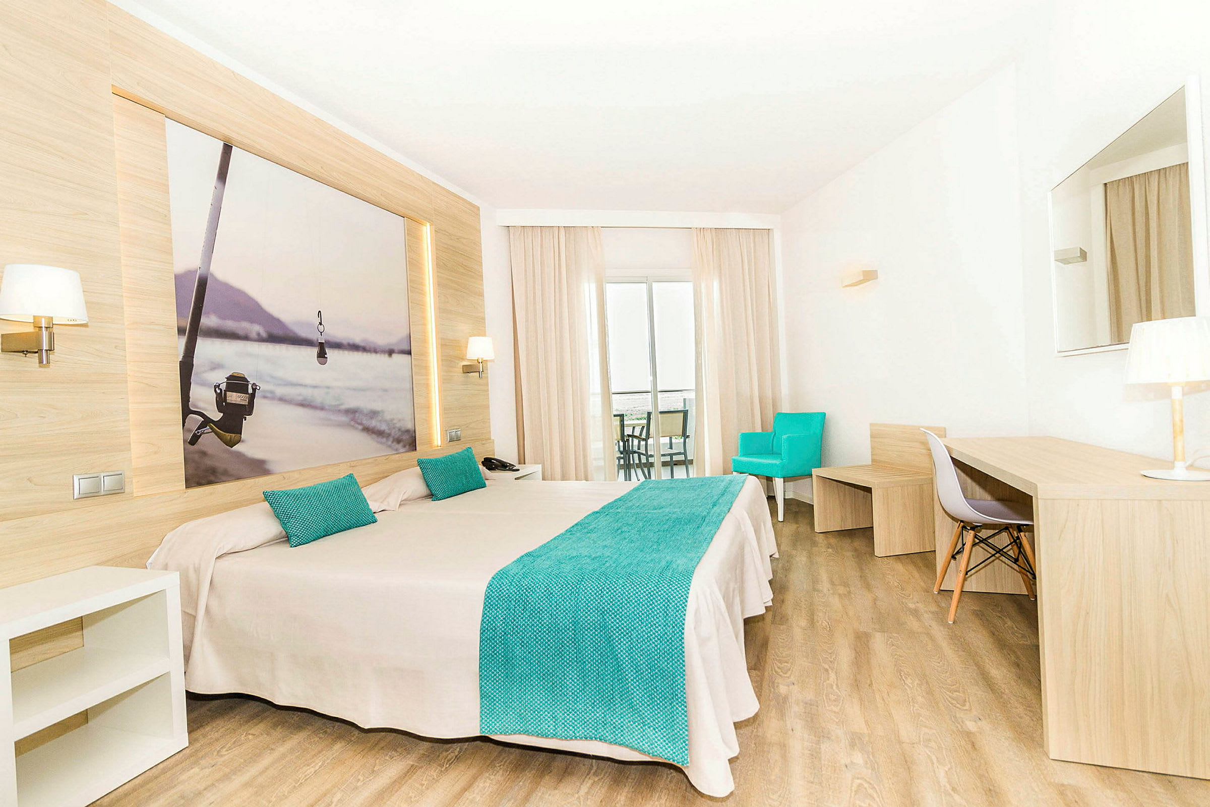Ett hotellrum med en dubbelsäng, turkosa detaljer och modernt trädesign. Bakom sängen hänger en tavla med ett fiske-tema. Rummet har ett skrivbord, en turkos fåtölj och en balkong. (AI-genererad text)