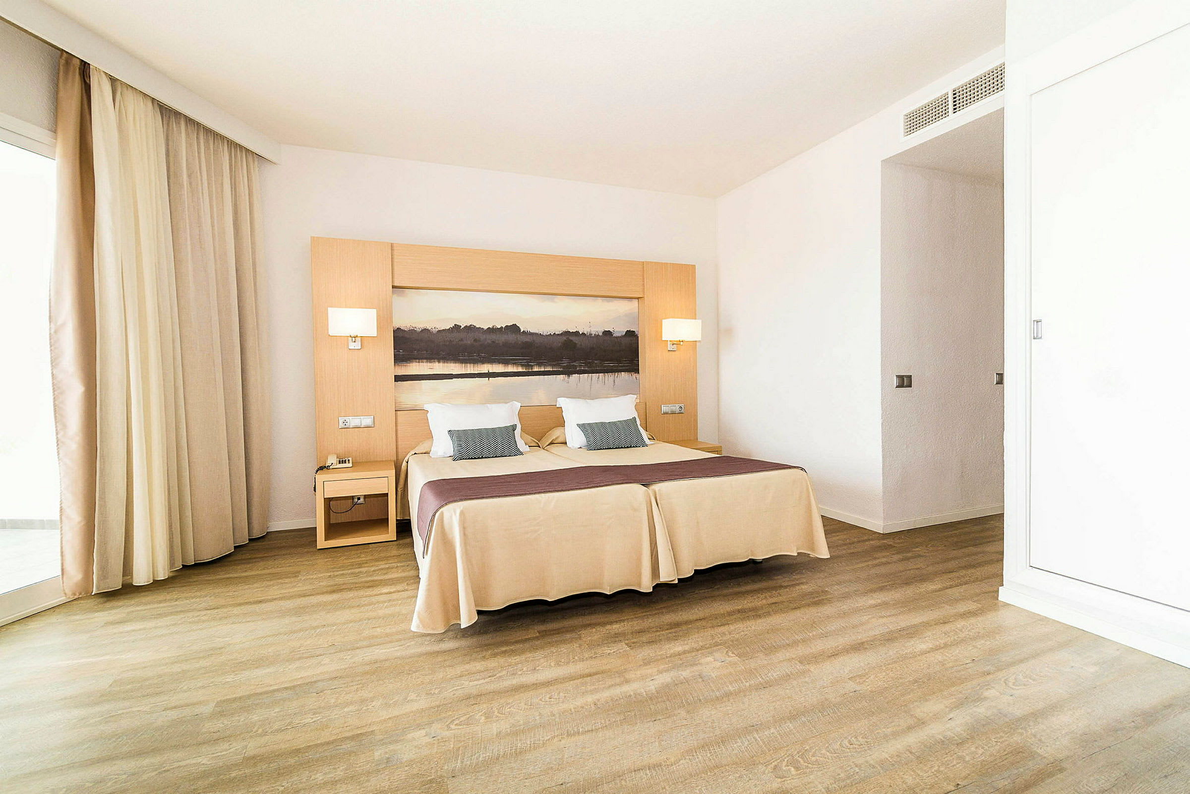 Ett hotellrum med en dubbelsäng, två sängbord, och en naturmålning bakom sängen. (AI-genererad text)