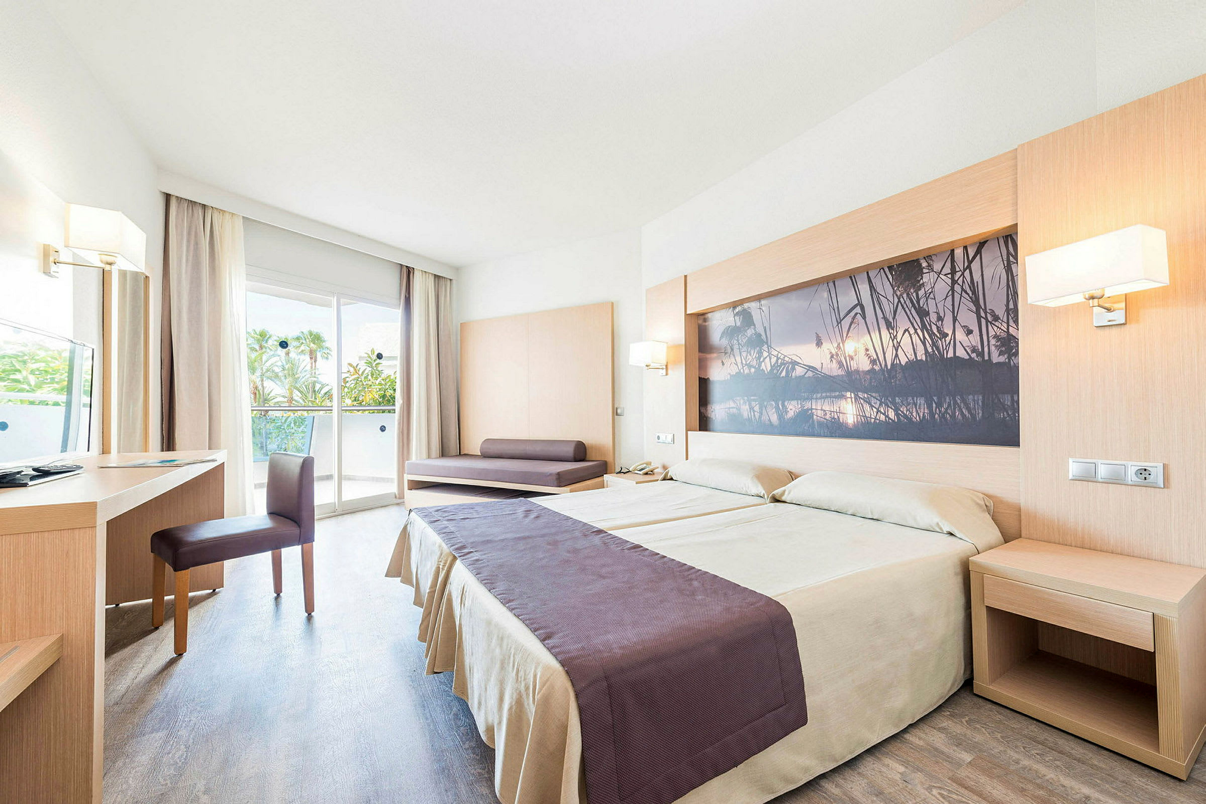 Ett hotellrum med en dubbelsäng, skrivbord, stol och en soffa. Rummet har en glasdörr som leder till en balkong. (AI-genererad text)