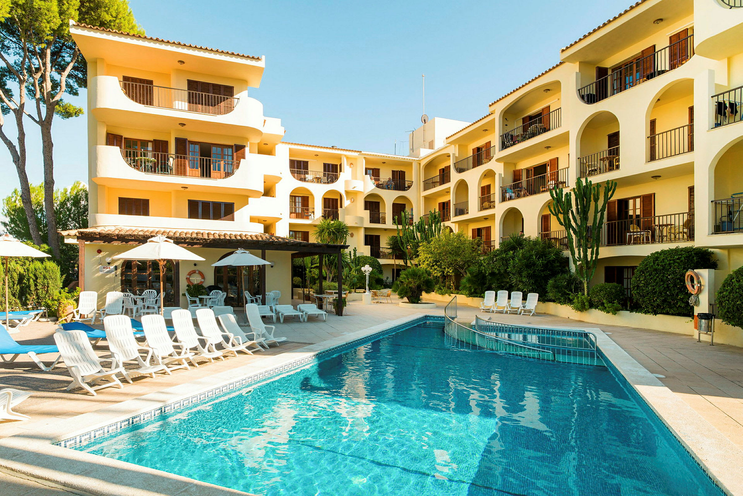 Ett hotell med balkonger och en pool bredvid solstolar och parasoller. (AI-genererad text)