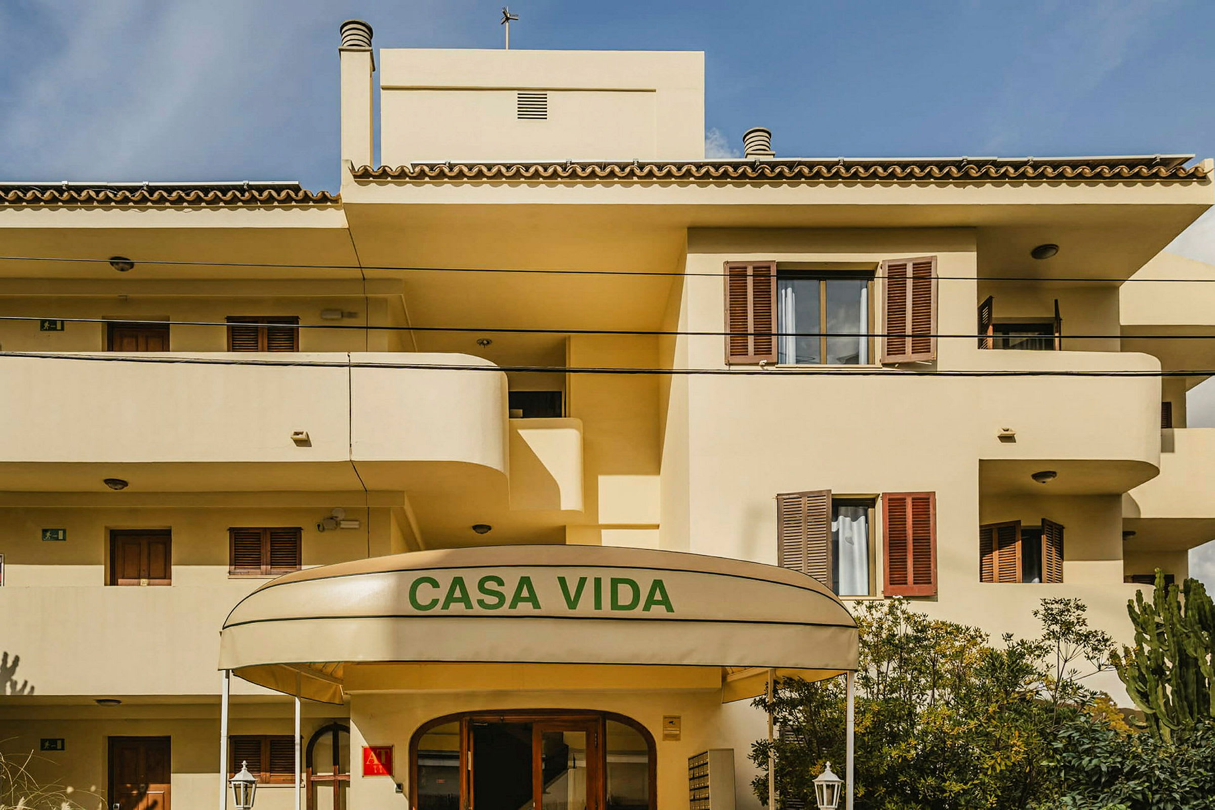 En gulmålad byggnad med balkonger och ett skydd ovanför entrén som har texten 'Casa Vida'. (AI-genererad text)