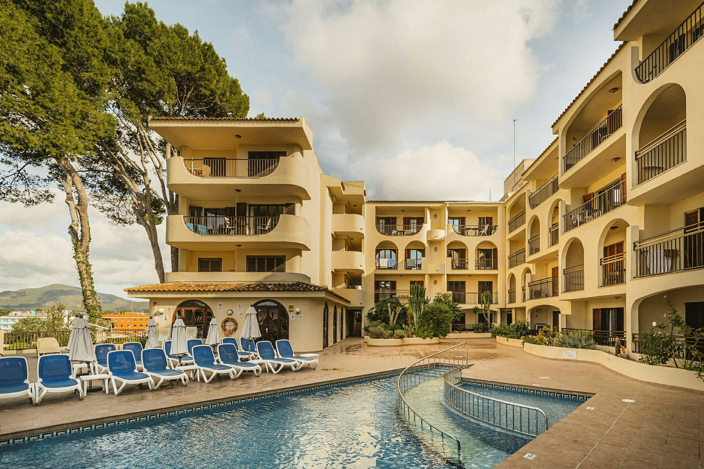 En bild av en hotellbyggnad med flera våningar, en pool och solstolar framför. (AI-genererad text)