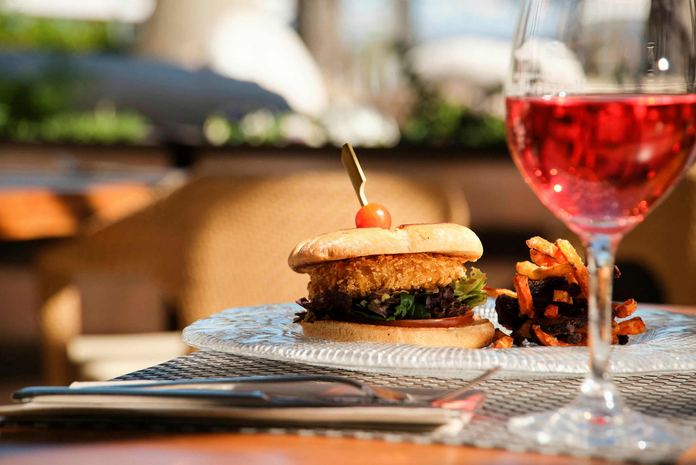 En tallrik med en hamburgare bredvid pommes frites och ett glas med rosévin. (AI-genererad text)