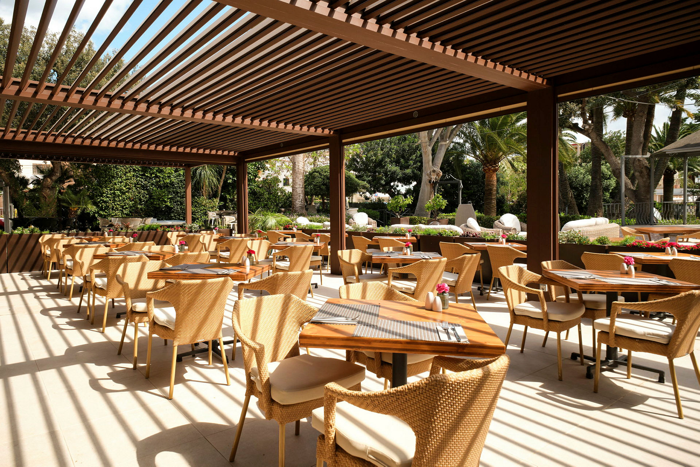 En utomhusrestaurang med bord och stolar och pergola. (AI-genererad text)