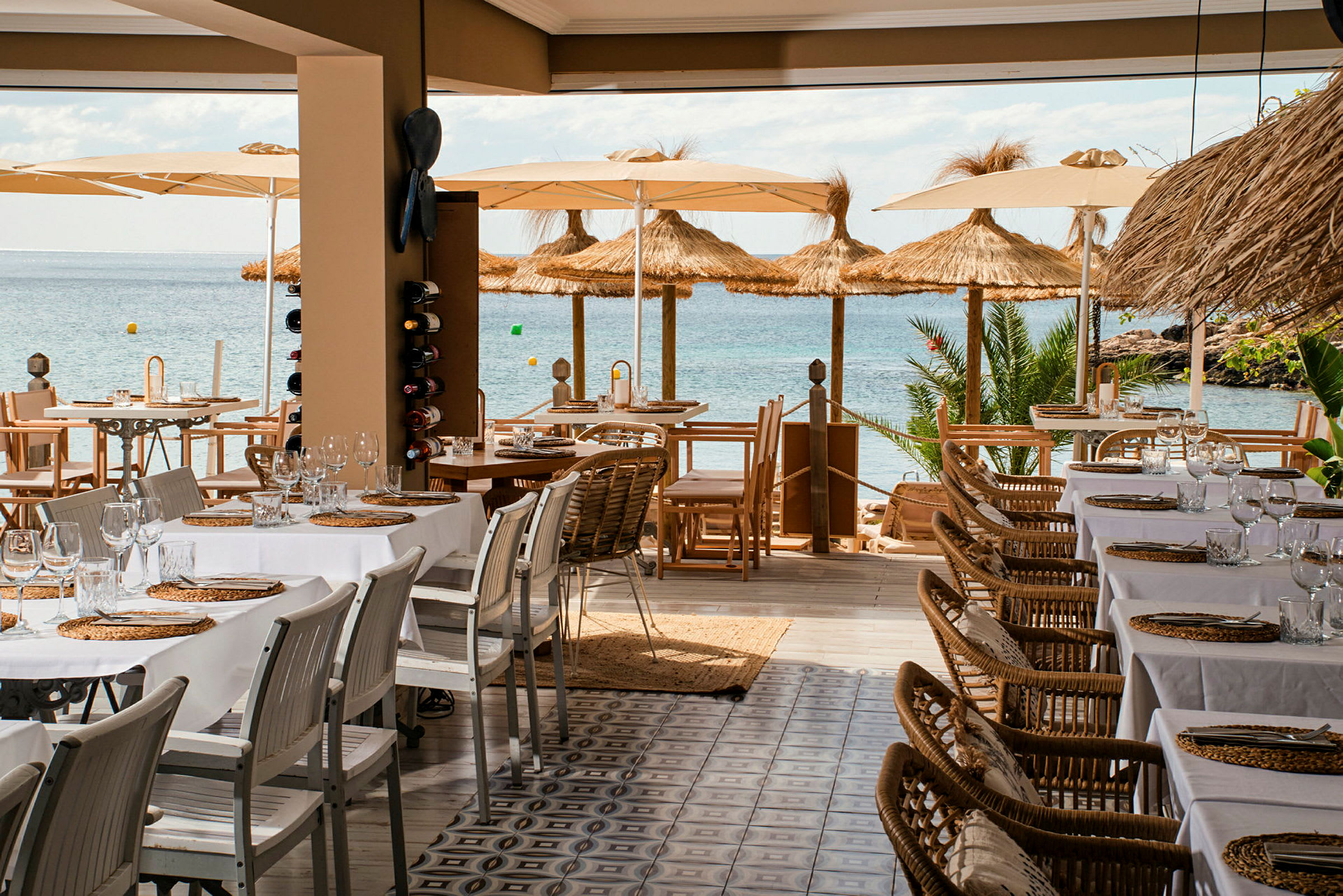Bild av en restaurang med dukade bord och utsikt över havet, parasoller och strandfront. (AI-genererad text)