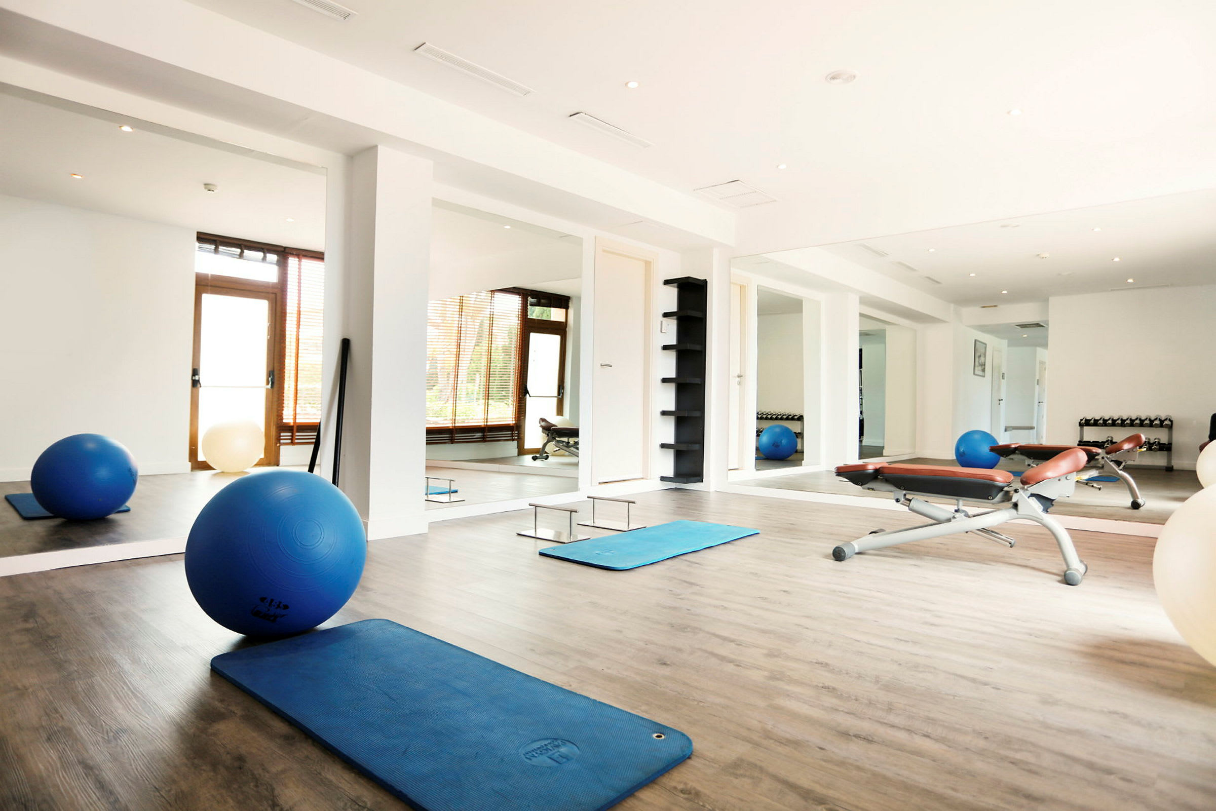 Ett ljust gym med träningsmattor, pilatesbollar och bänkar. (AI-genererad text)