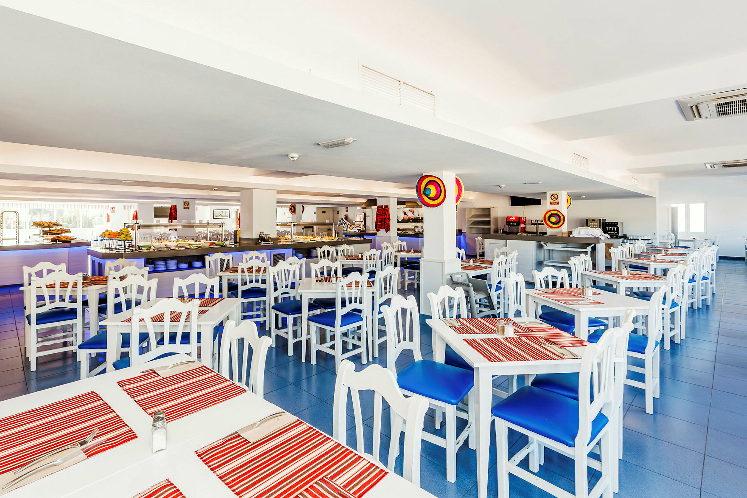 Interiör av en restaurang med vita bord och stolar med blåa dynor samt röda randiga bordstabletter. (AI-genererad text)