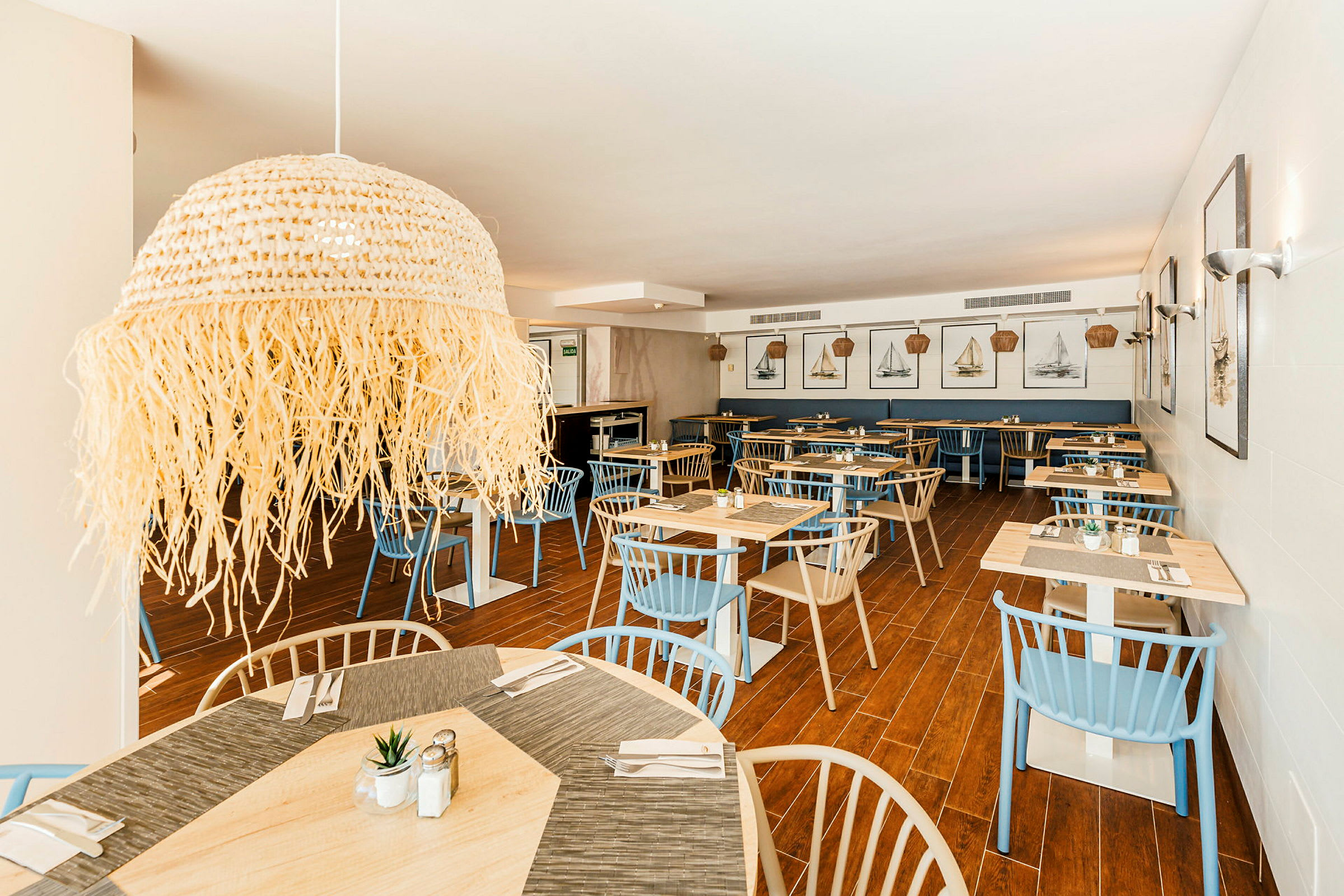Interiör av en restaurang med träbord, blå och beige stolar samt väggdekorationer med båtmotiv. (AI-genererad text)