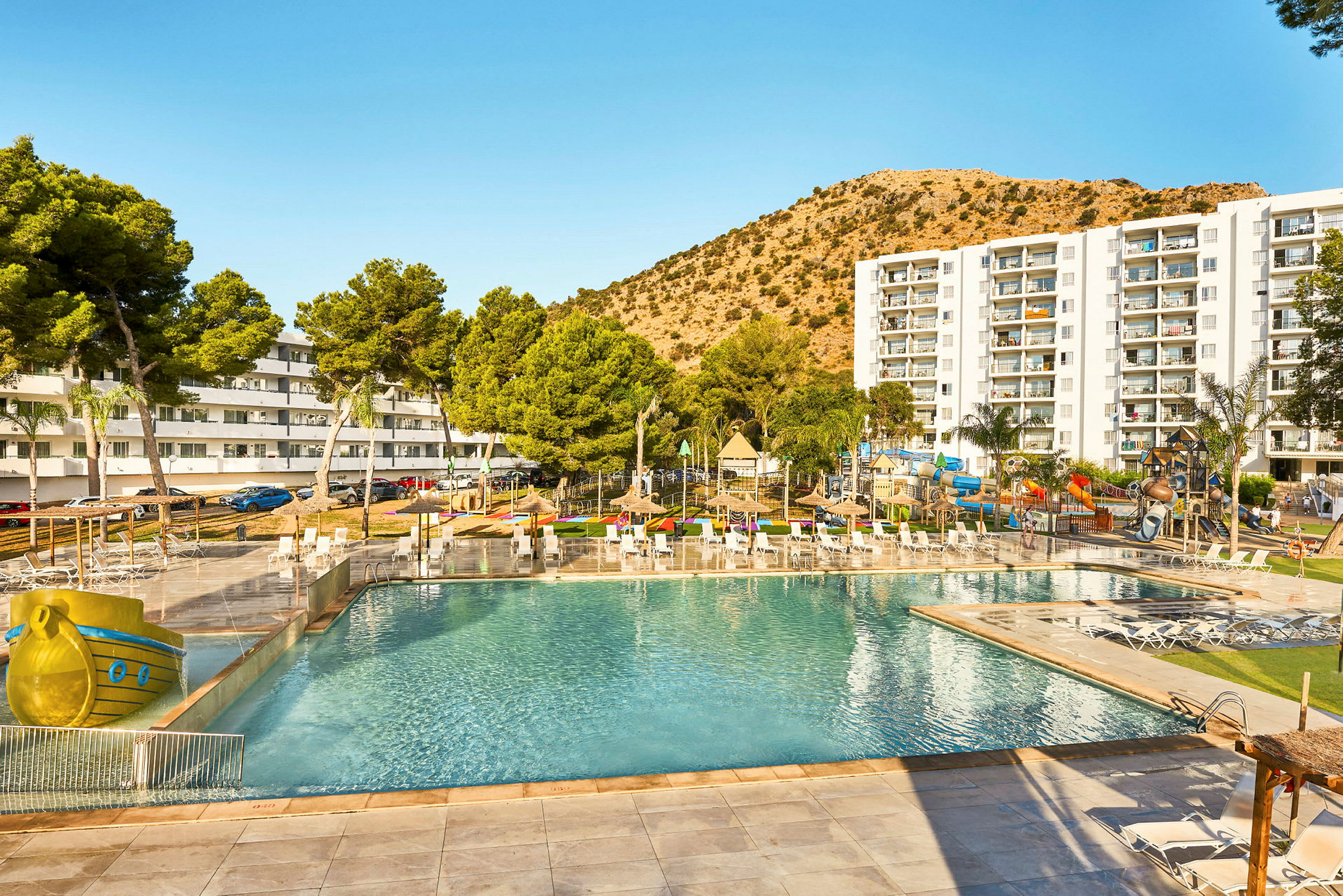 Semesterhotell med poolområde, solstolar, och en lekplats för barn i en solig miljö. (AI-genererad text)